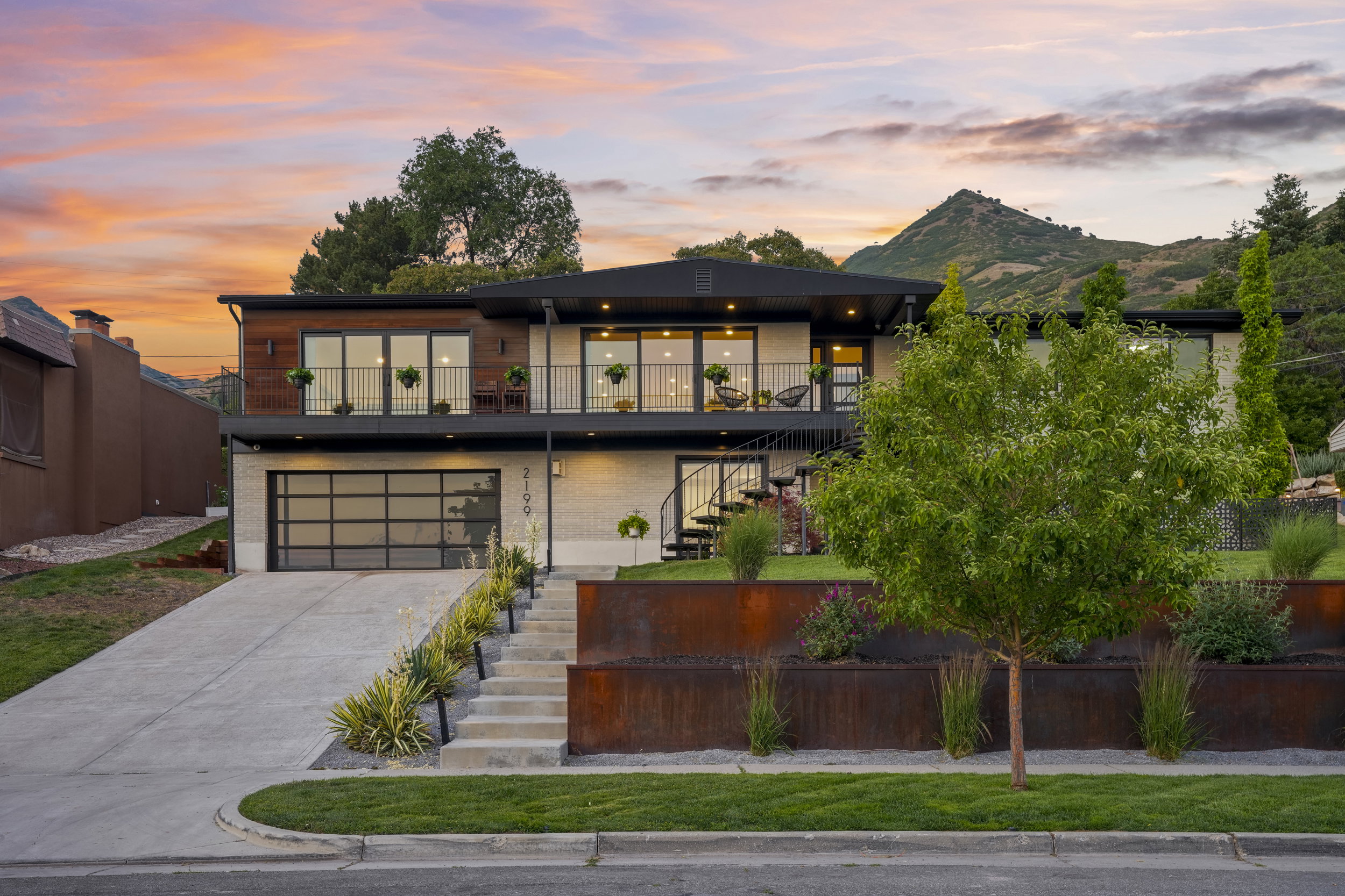 Contemporary multi-level residence featuring a two-car garage with a glass-paneled door, upper-level balconies with metal railings, and wood-paneled accents