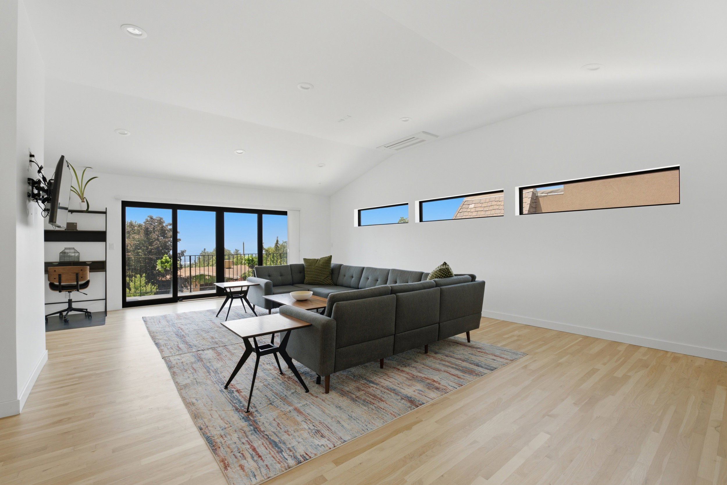 Spacious living area featuring light wood-finish flooring, vaulted ceilings, and recessed lighting
