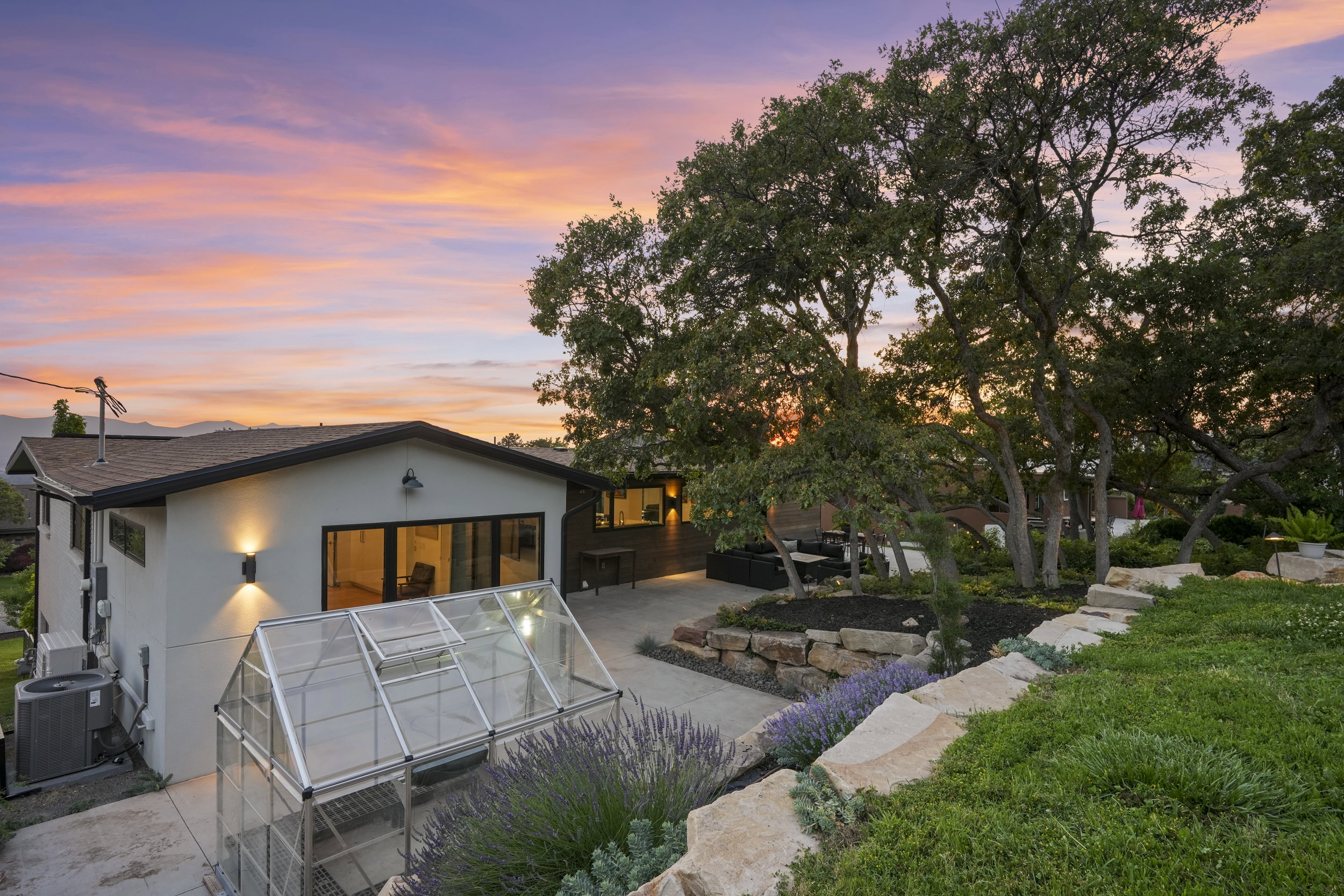 Exterior showcasing a modern greenhouse, an outdoor patio space, and mature trees
