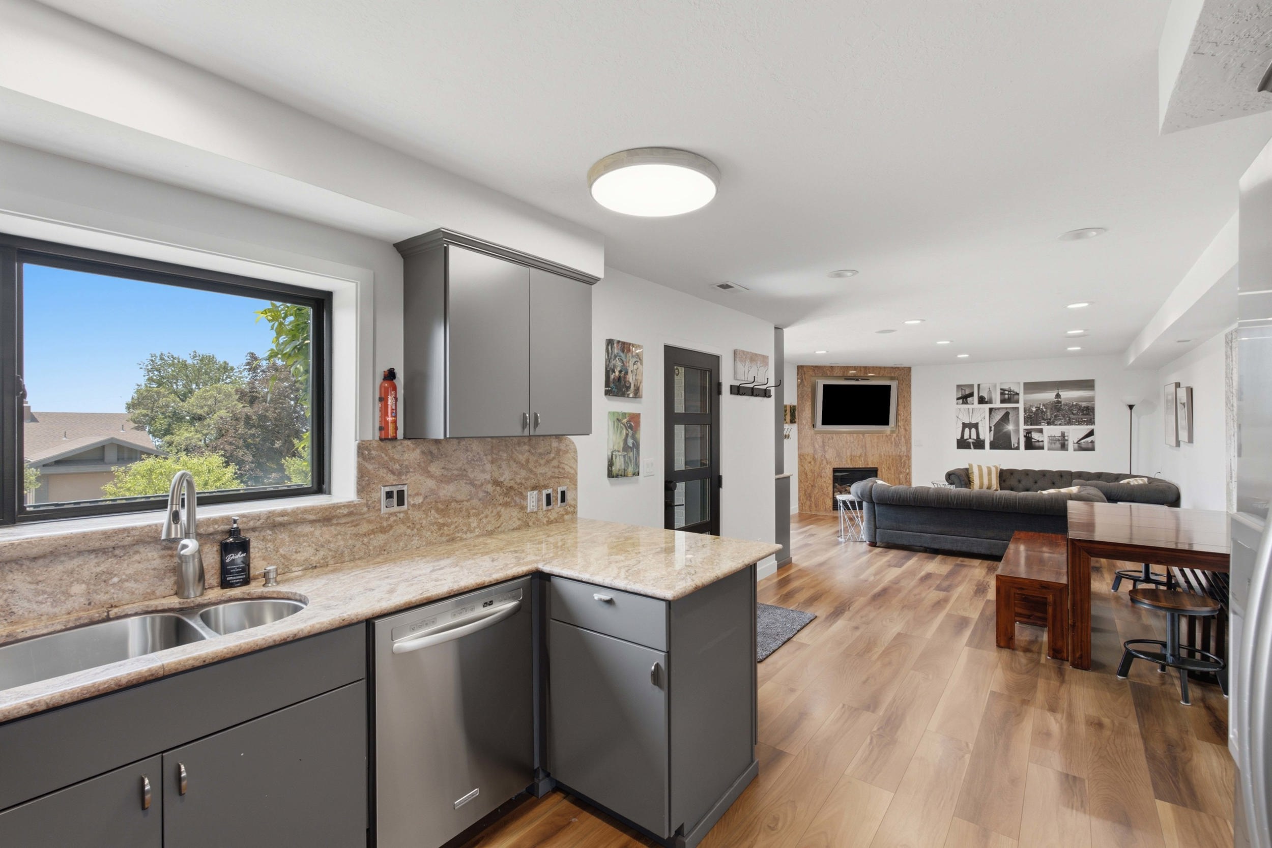 Kitchen area featuring gray cabinetry with brushed nickel hardware, light-toned stone countertops, and a dual basin stainless steel sink with a gooseneck faucet