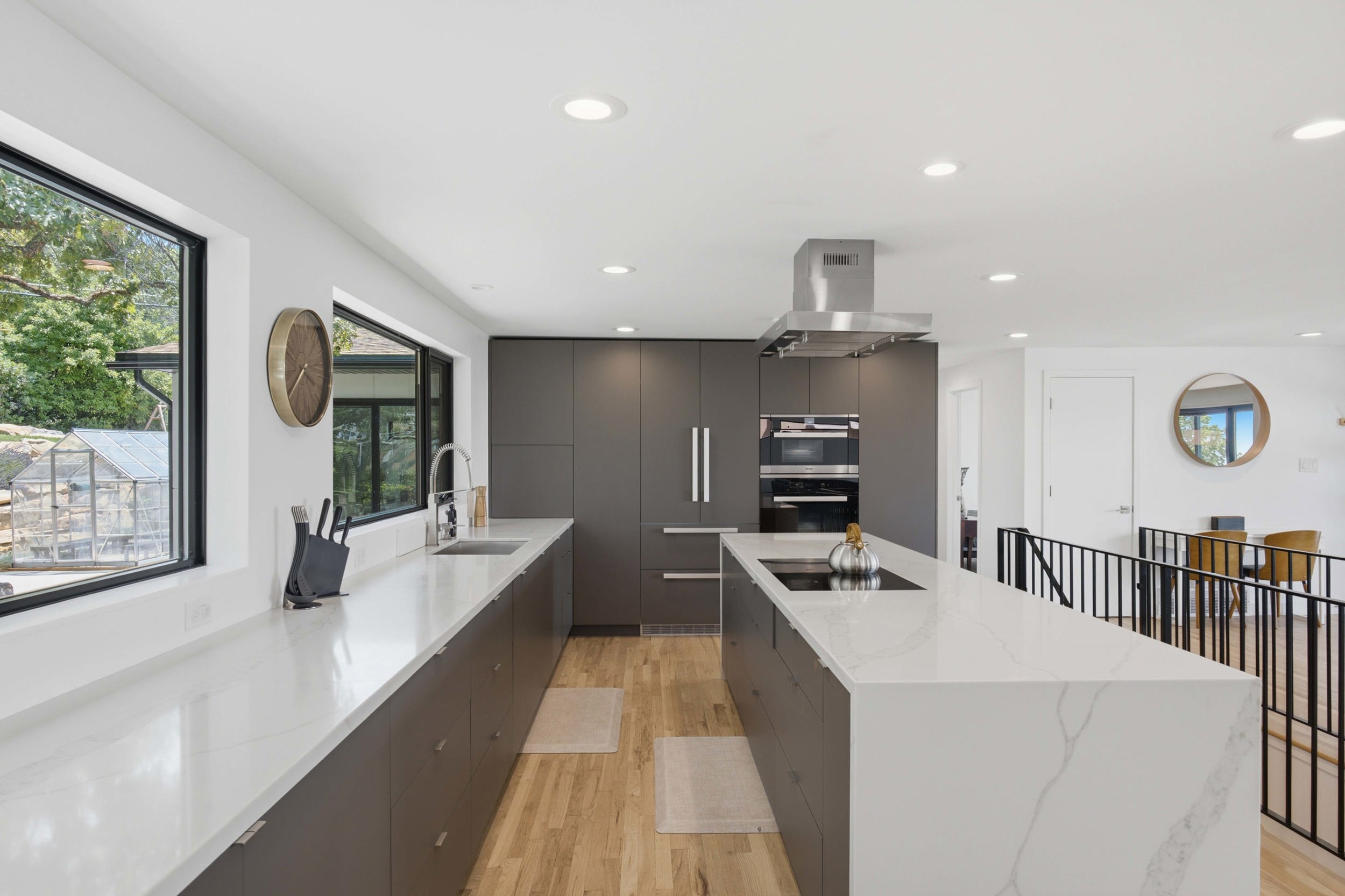 Modern kitchen featuring an extended island with a cooktop, stone countertops, integrated stainless steel appliances, and wood-finish flooring