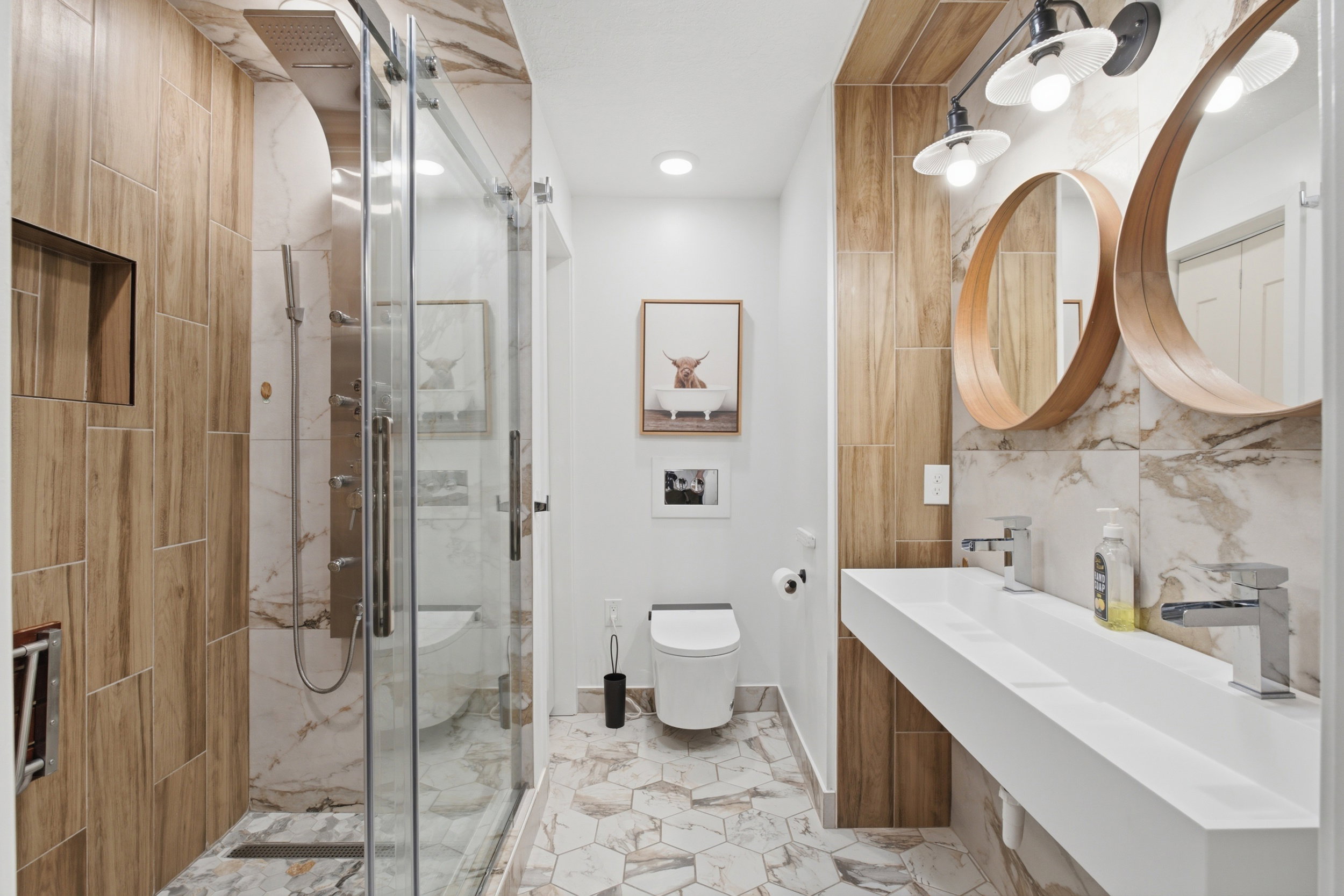 Contemporary bathroom featuring a floating dual vanity with vessel sinks, two circular mirrors, and a glass-enclosed shower with a rainfall showerhead
