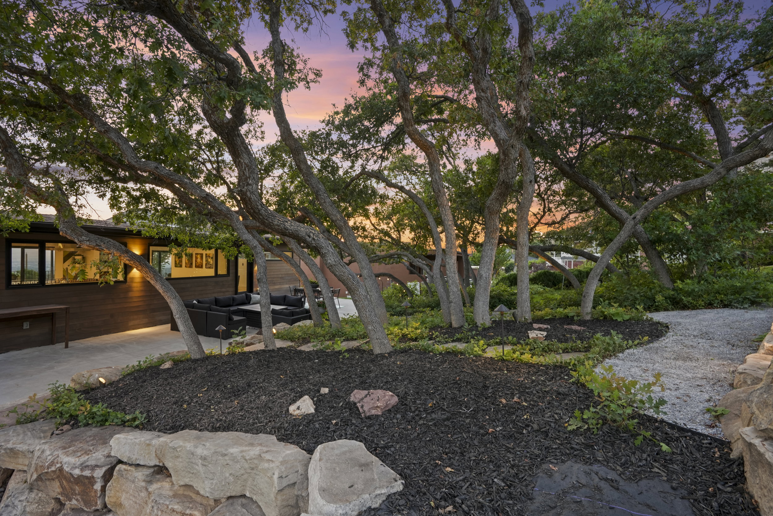 Expansive outdoor living area featuring multiple mature trees, a gravel pathway, and a stone retaining wall