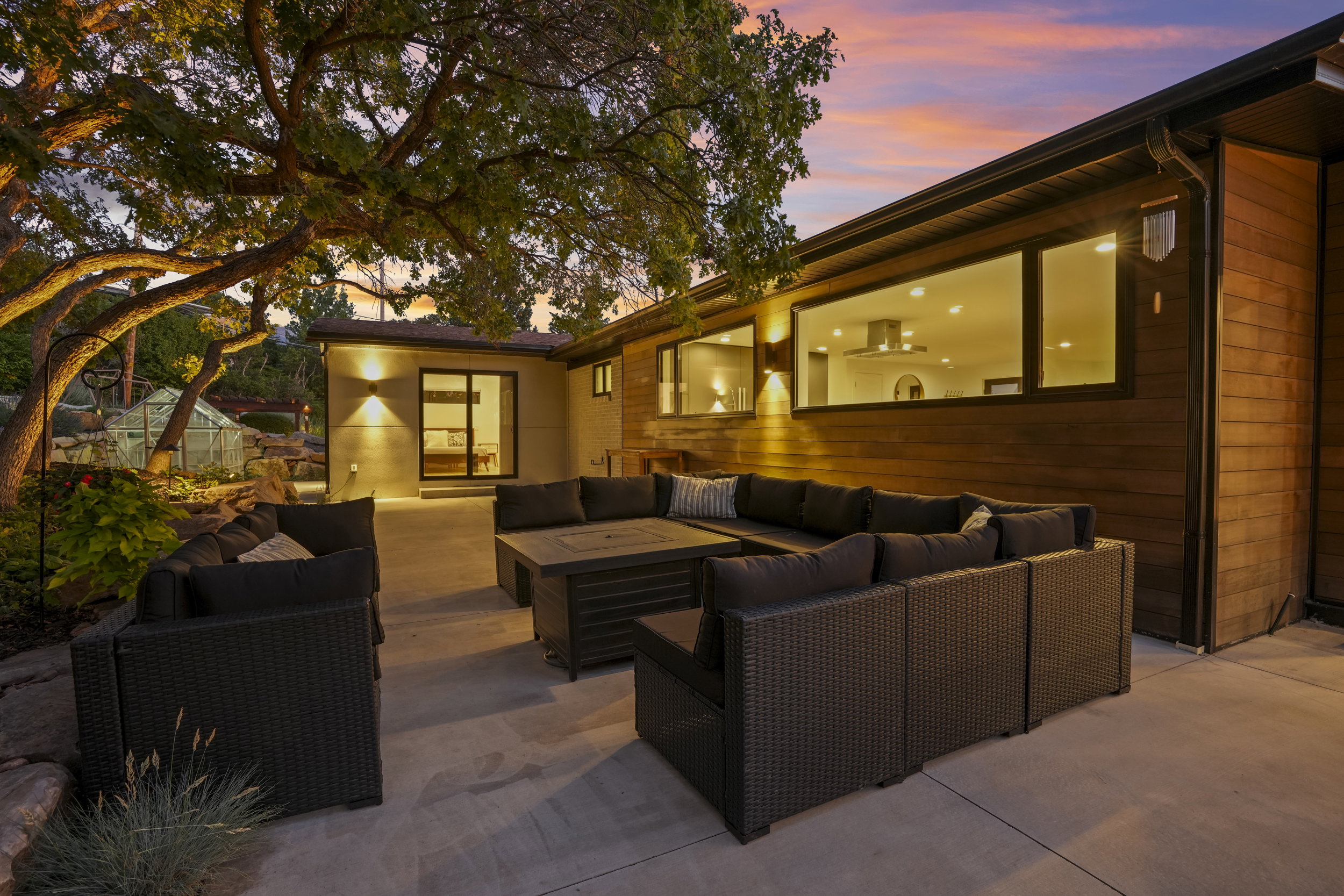 Expansive rear patio featuring a concrete surface, mature tree landscaping, and a greenhouse structure