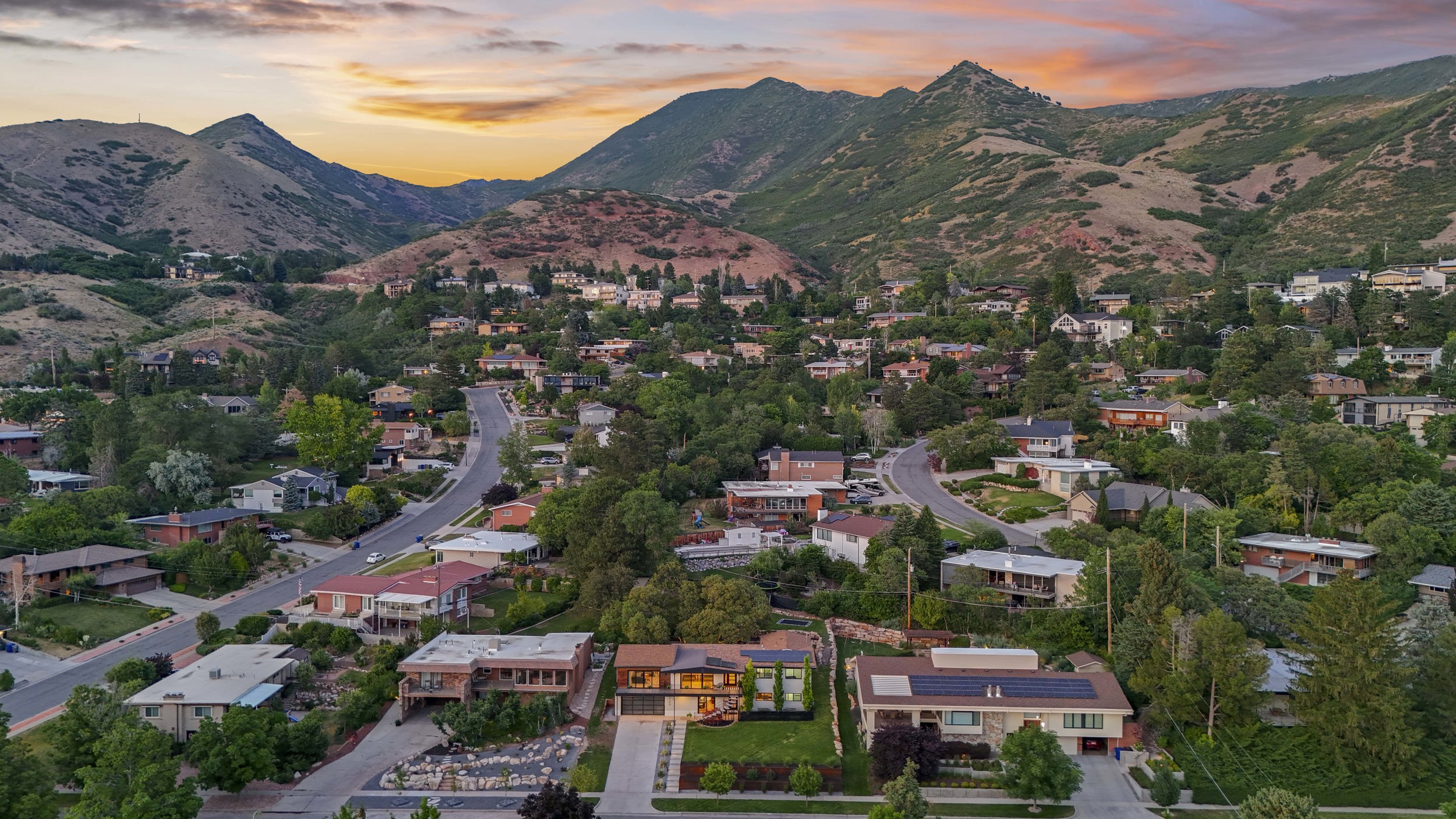 Residential area situated in a mountain valley, featuring mature trees and a curving roadway