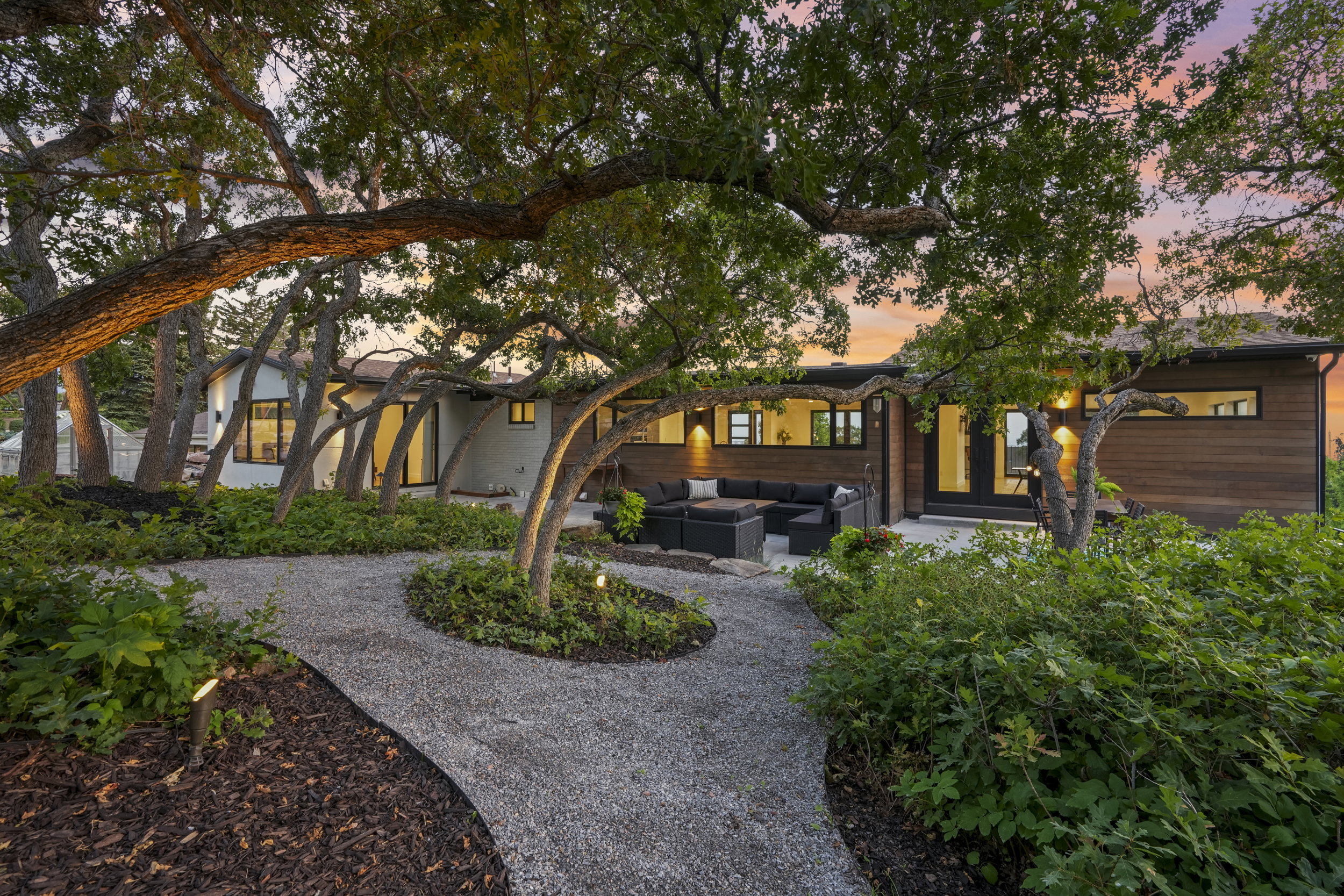 Exterior featuring a private pea gravel path, mature trees, landscaped grounds, a spacious patio, and a contemporary facade with wood-finish siding and numerous windows