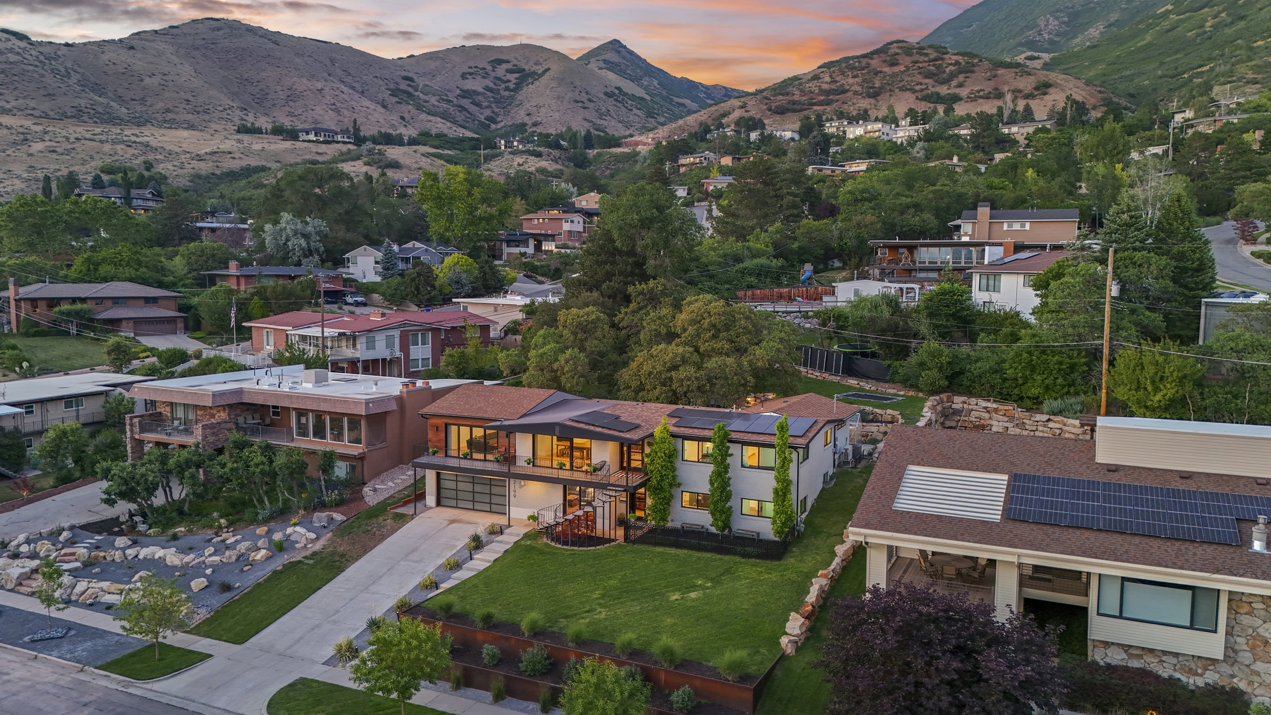 Contemporary residence featuring a terraced front yard with manicured lawn, a concrete driveway, and integrated solar panels