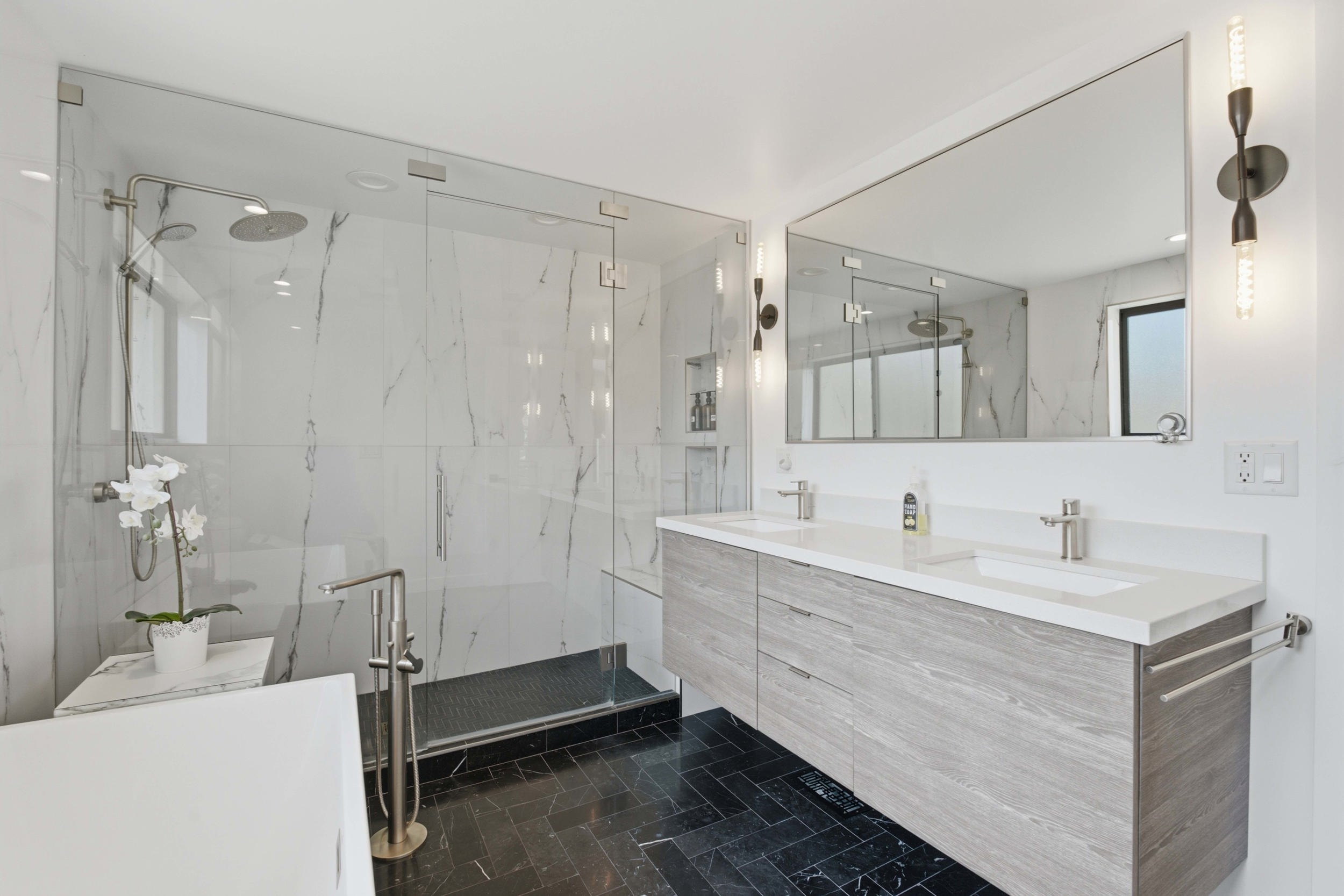 Modern bathroom featuring a dual vanity with light wood-finish cabinetry and white countertops