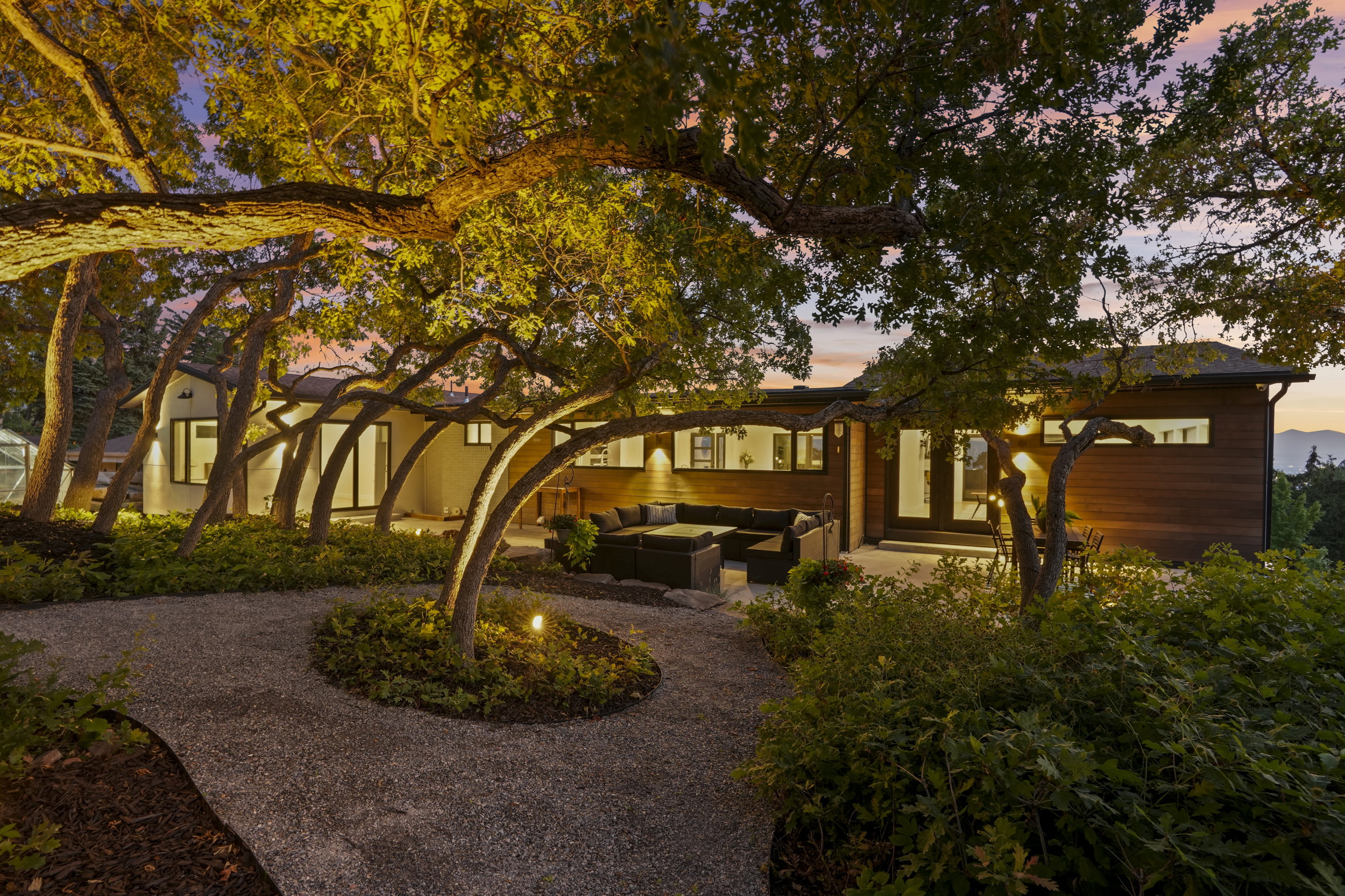 Exterior featuring wood siding, a gravel pathway with integrated landscape lighting, and mature trees