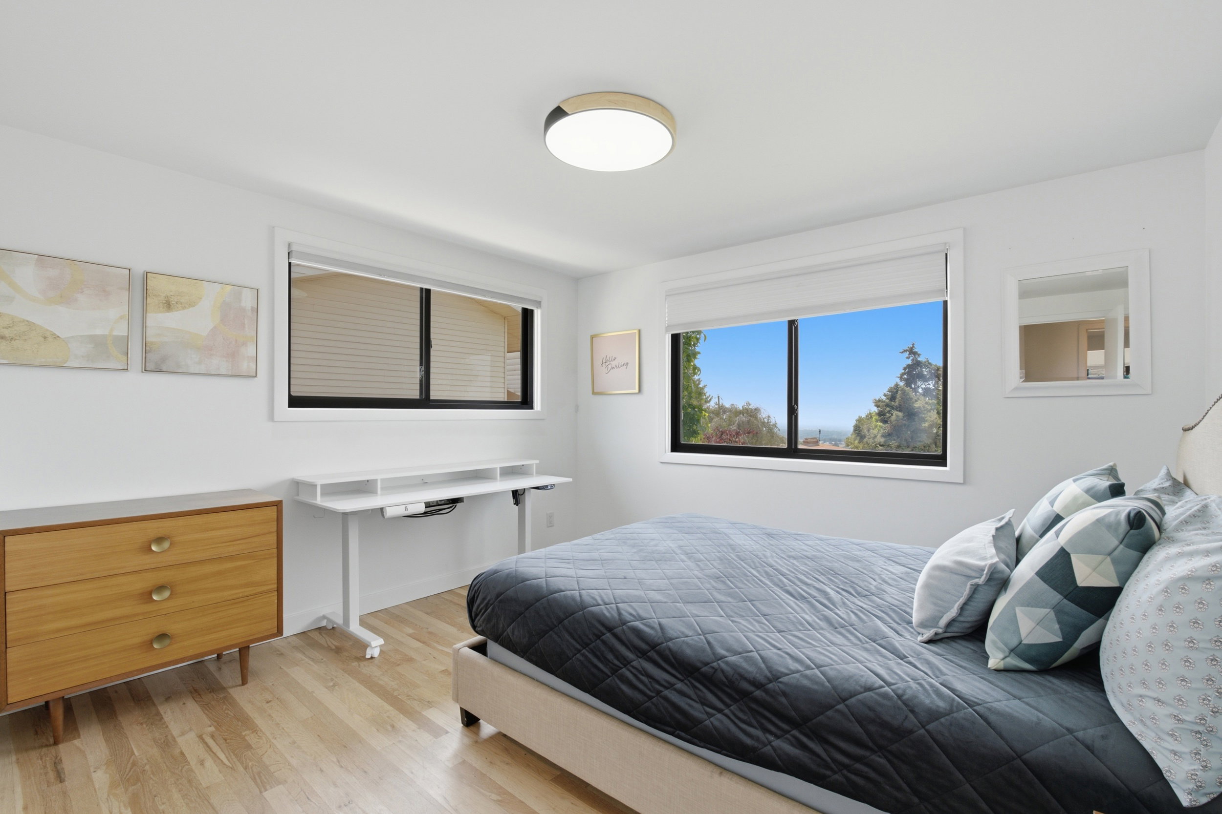 Light wood-finish flooring complements the bright white walls of this bedroom, featuring two large windows with black frames