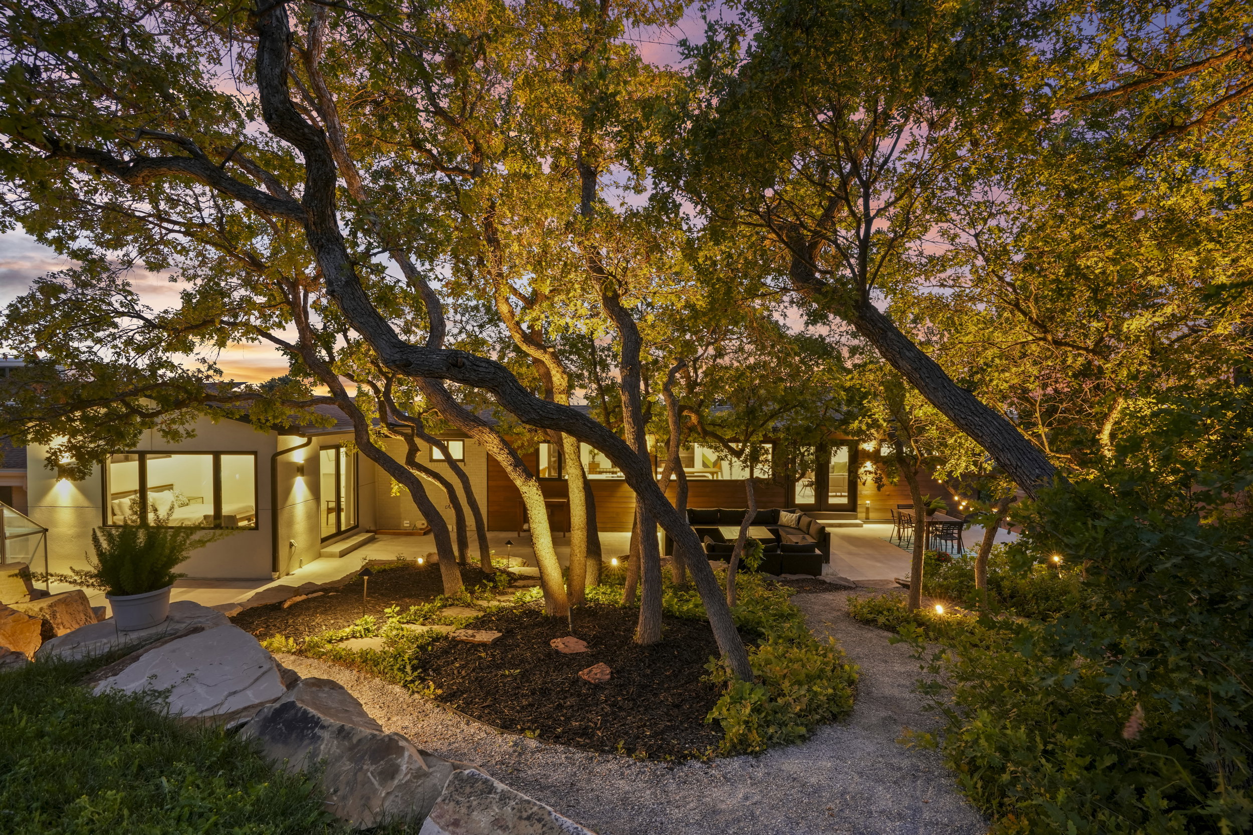 Landscaped outdoor area featuring mature trees, a gravel pathway, and integrated ground lighting
