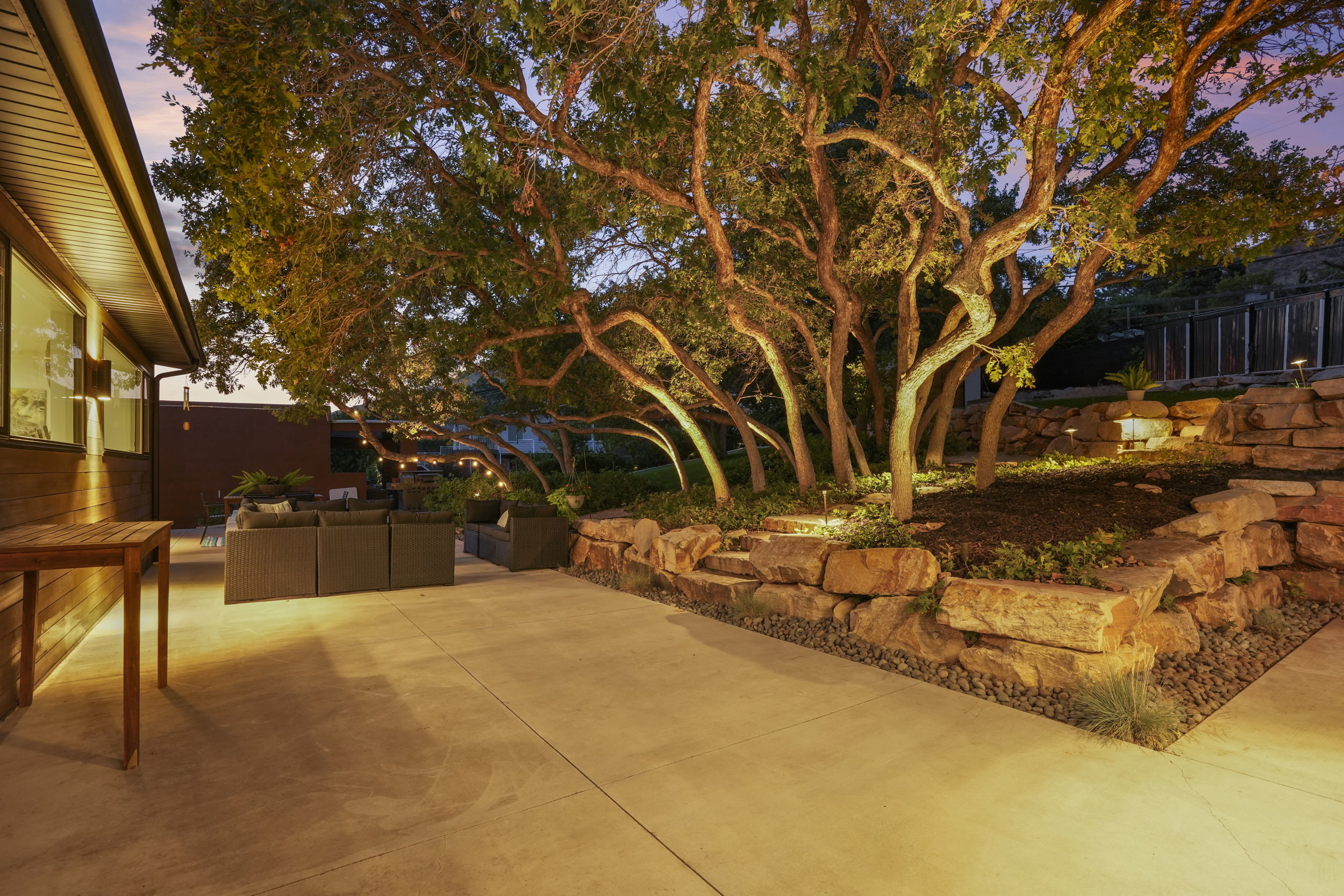 Expansive concrete patio bordered by a natural stone retaining wall and mature trees