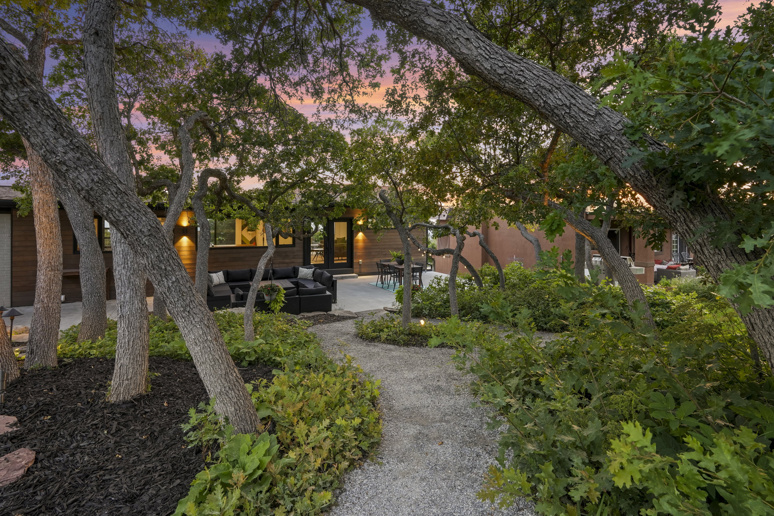 Landscaped outdoor area featuring a gravel pathway, mature trees, and planted greenery