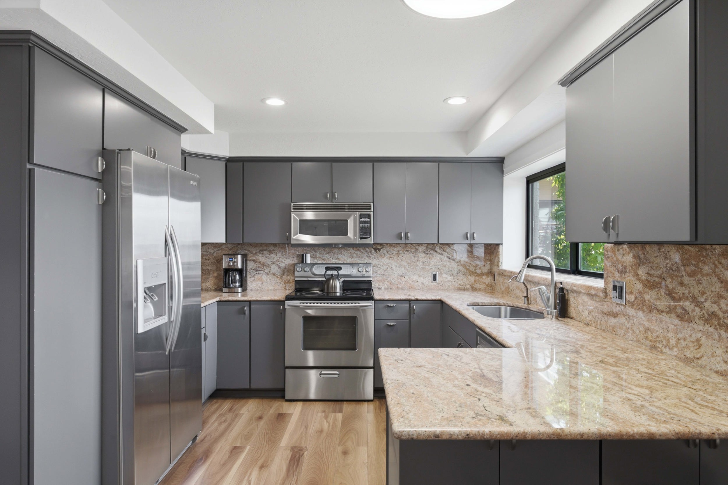 Modern kitchen featuring gray cabinetry, stainless steel appliances, and light-toned stone countertops