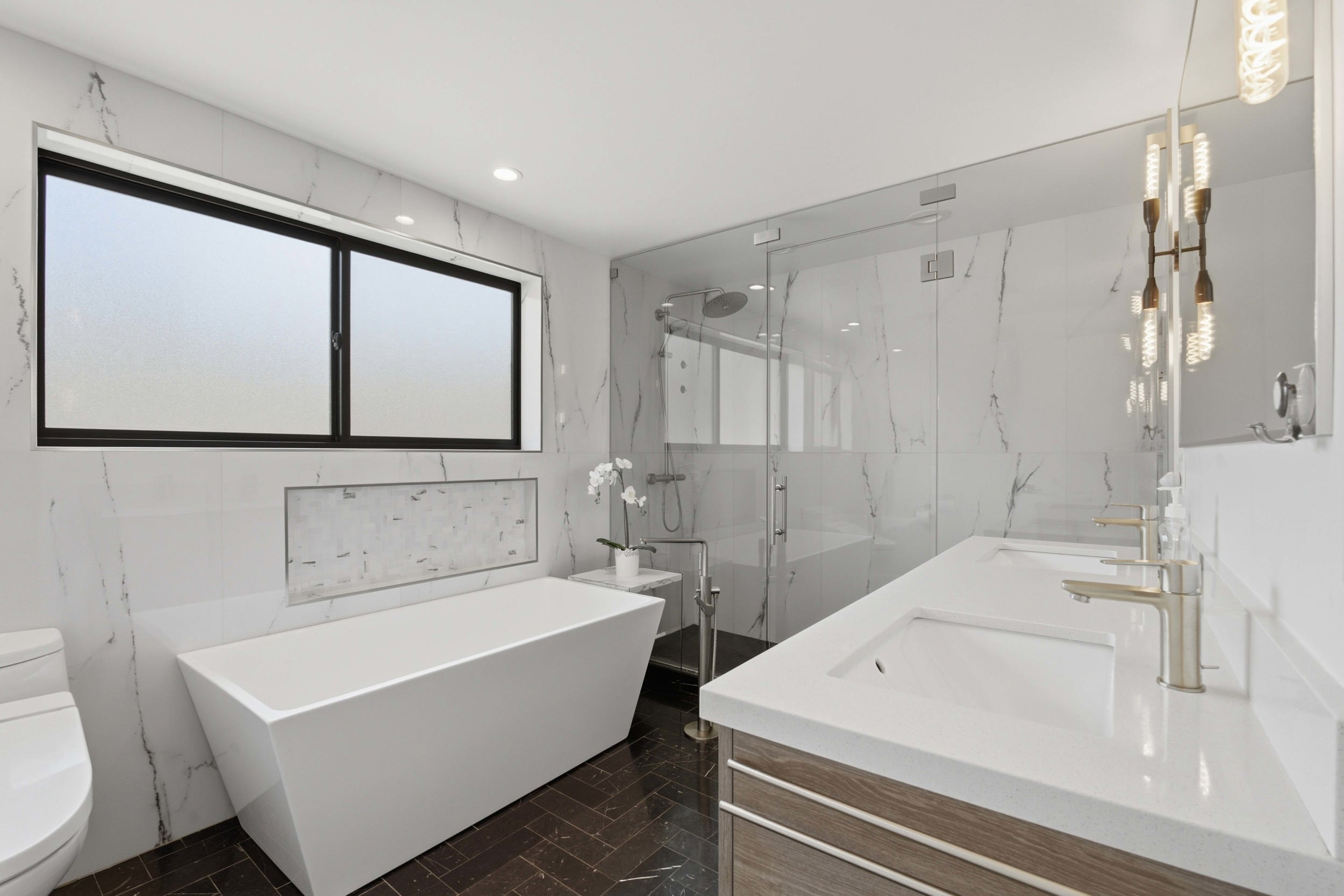 Bathroom featuring a freestanding soaking tub, dual vanity with undermount sinks, glass-enclosed shower, and herringbone-patterned floor