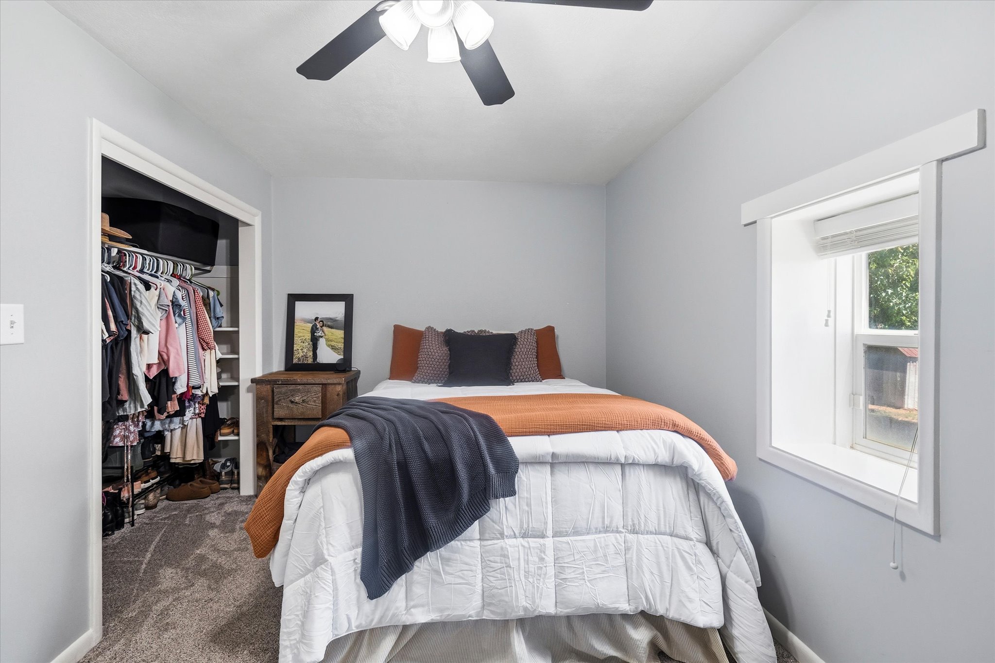 Bedroom featuring a ceiling fan with light fixture, gray carpeting, a built-in closet with shelving, and a window with white trim
