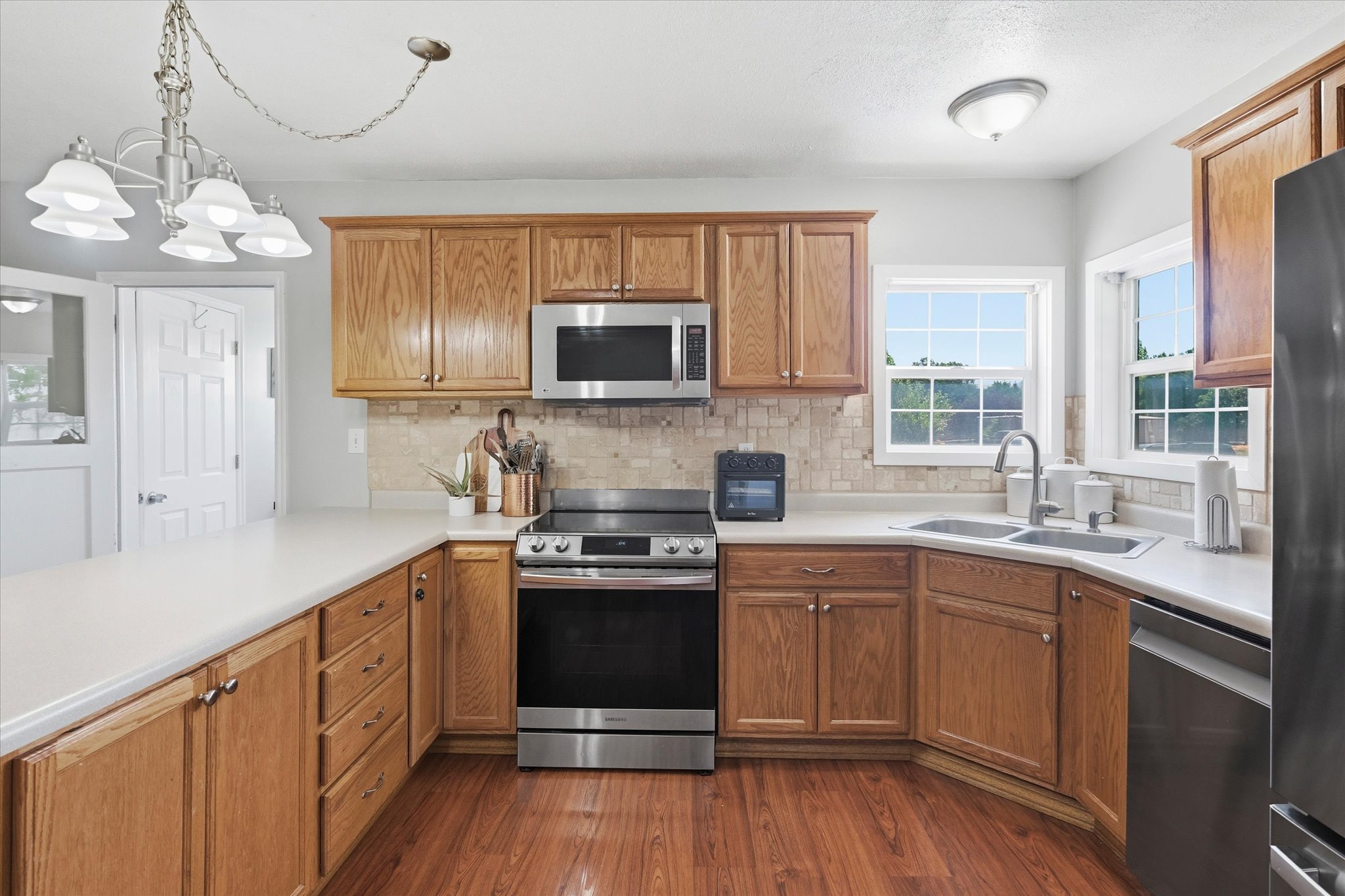 Spacious kitchen featuring wood-finish flooring, light wood cabinetry, light countertops, a stainless steel range, and a dual-basin sink with a window overhead
