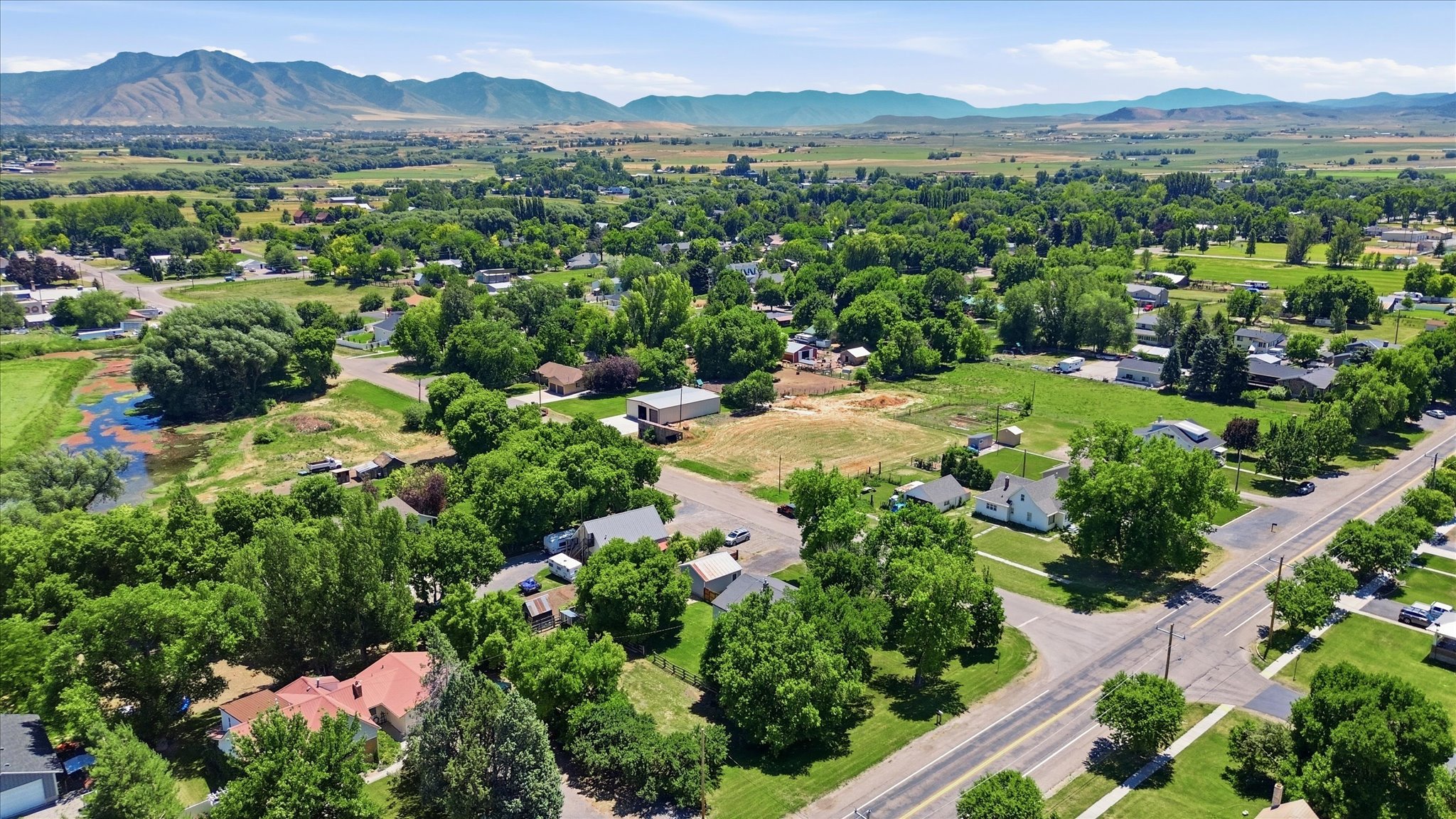 Expansive rural landscape featuring a mix of residential properties, abundant mature trees, and mountainous terrain in the distance