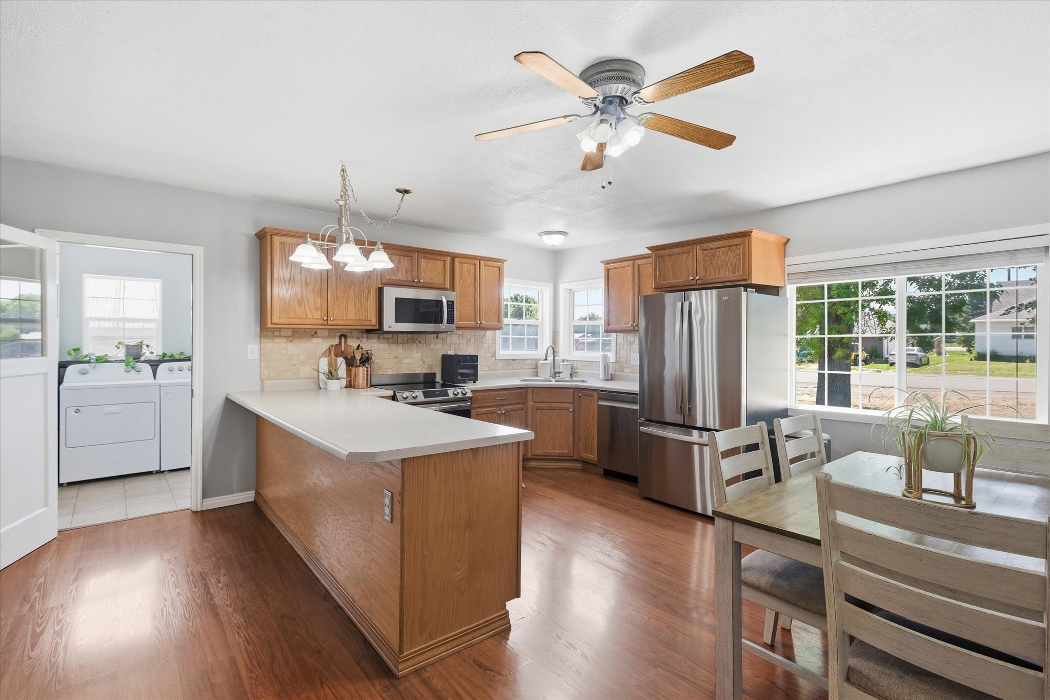 Open-concept kitchen featuring wood-finish flooring, wood cabinetry, stainless steel appliances, and a central island with a light-colored countertop