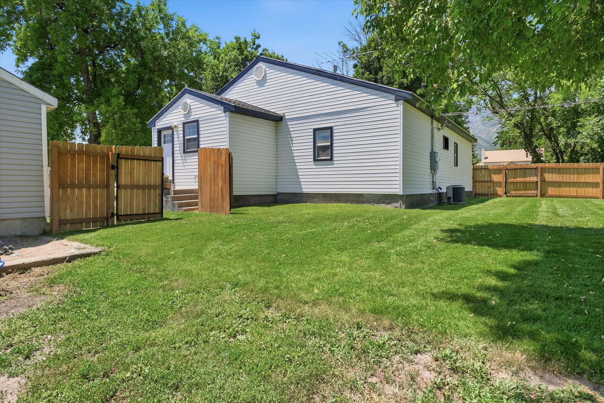 Expansive yard space featuring a white siding exterior, new wood fencing, concrete steps, and a detached structure
