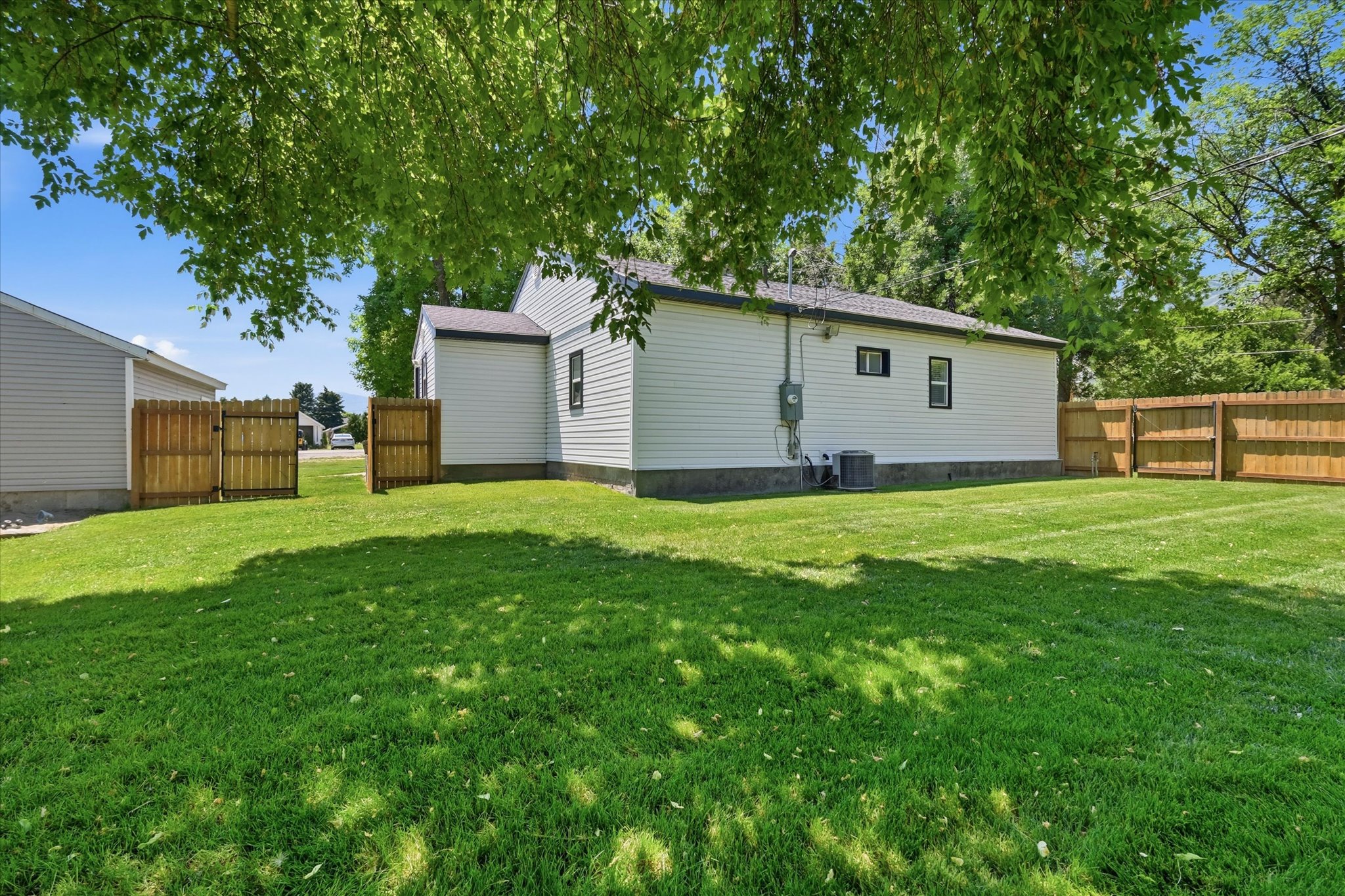Spacious backyard featuring white siding, a full wood fence, and mature trees