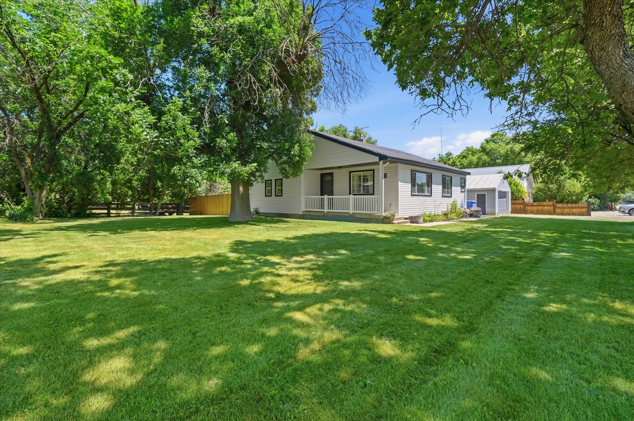 Expansive front yard featuring a manicured lawn, mature shade trees, and a white picket fence