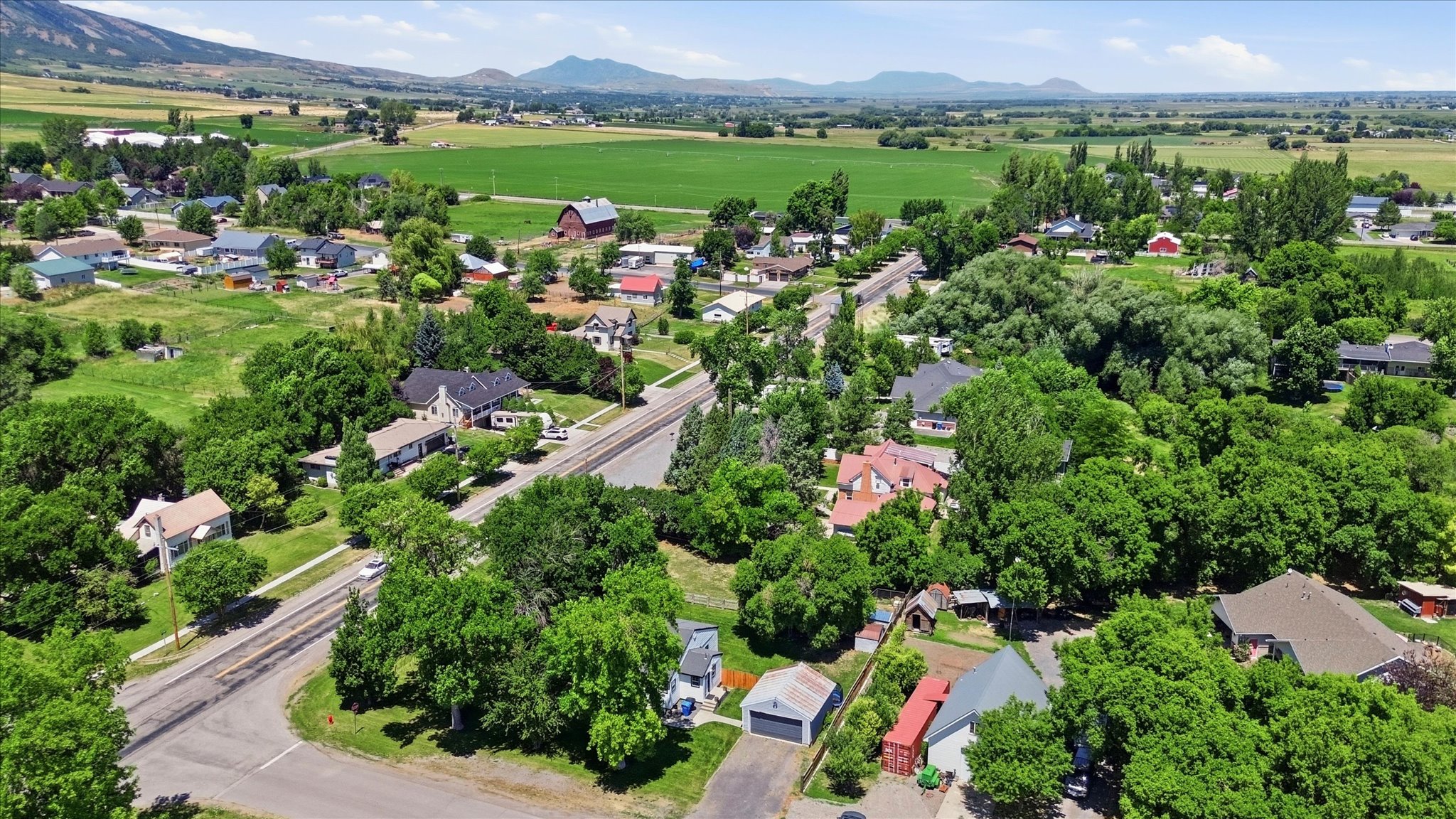 Expansive aerial capturing a rural community surrounded by green fields and distant mountains