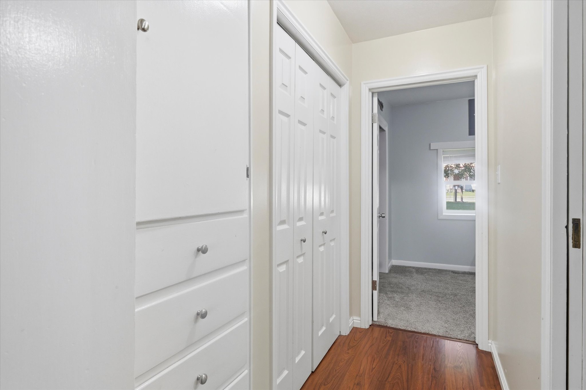 Hallway featuring wood-finish flooring and integrated white cabinetry with silver hardware