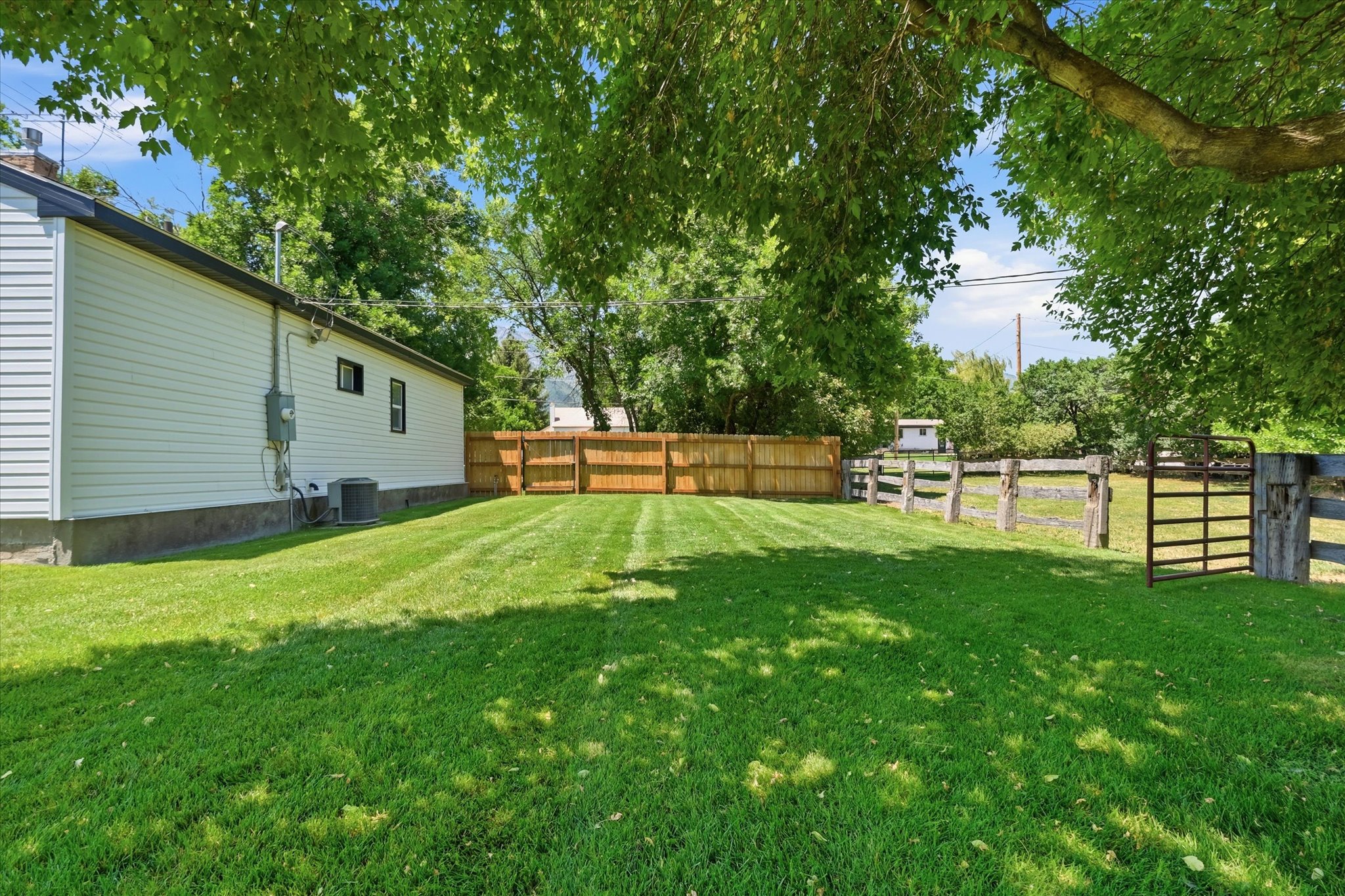 Spacious green lawn with wood privacy fencing, a split-rail fence, and a metal gate