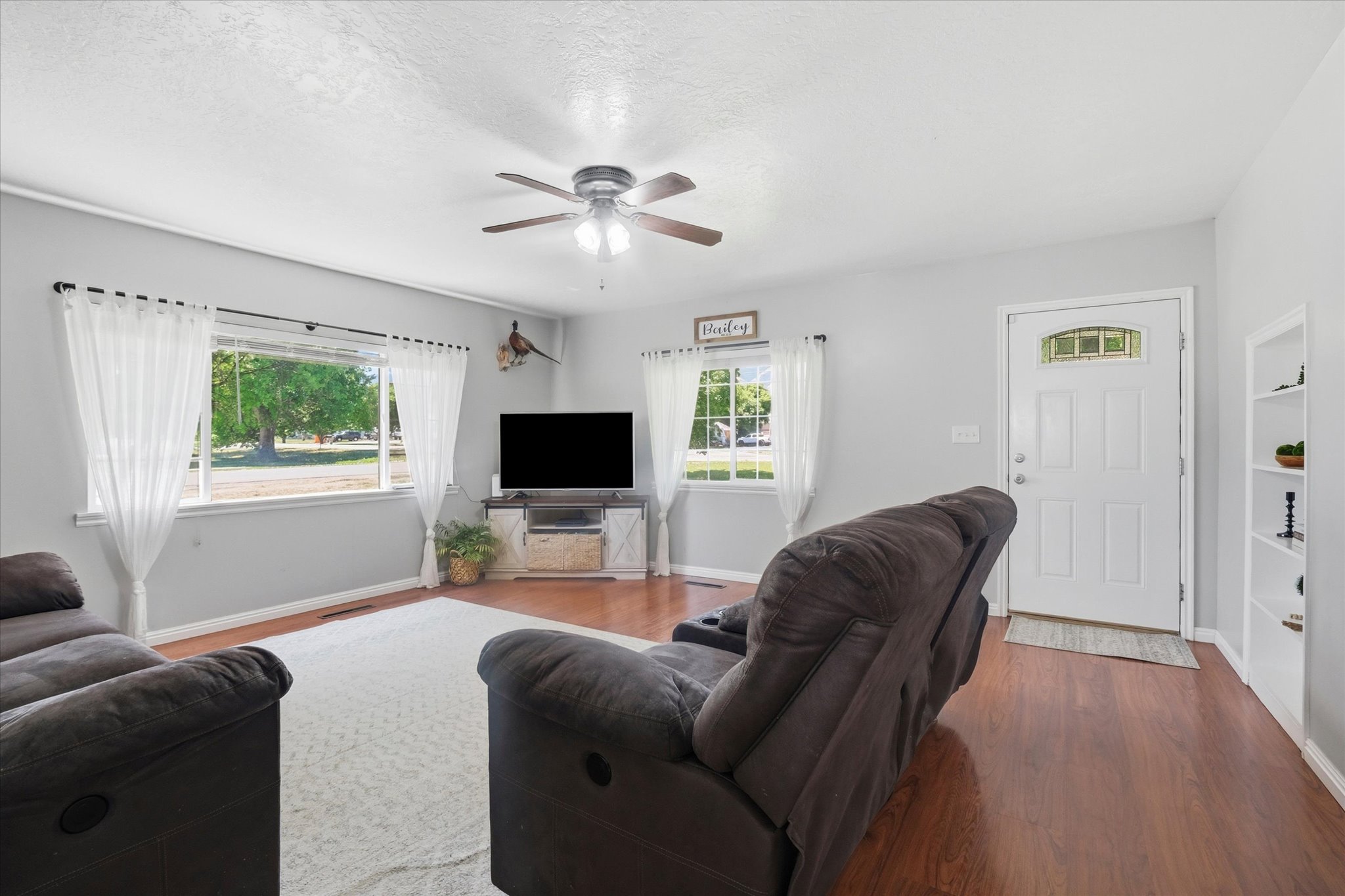 Living area featuring wood-finish flooring, light gray wall paint, and a ceiling fan with integrated lighting