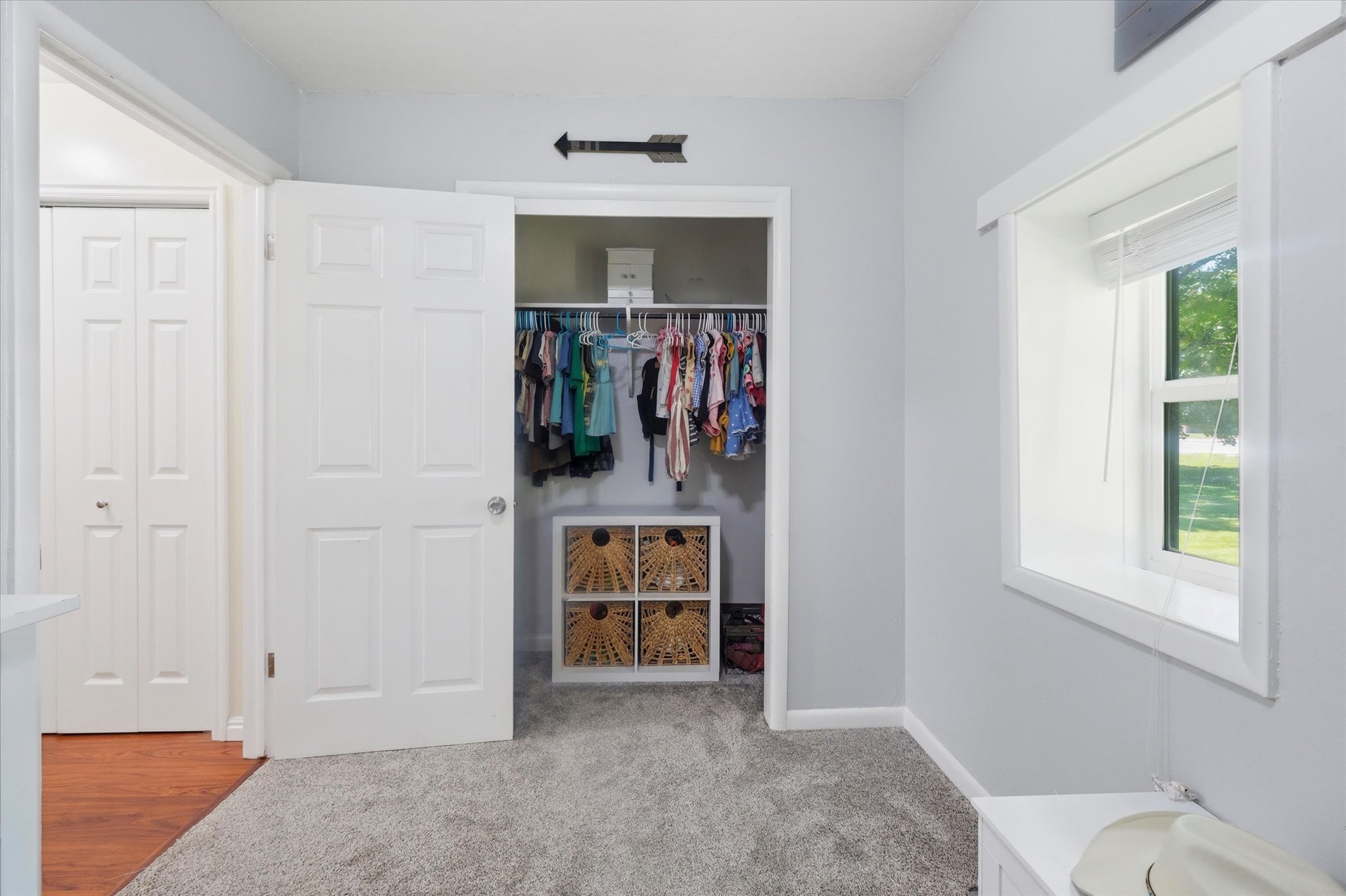 Carpeted room with a window featuring white trim and blind, a closet with a white door, and a second white bi-fold door