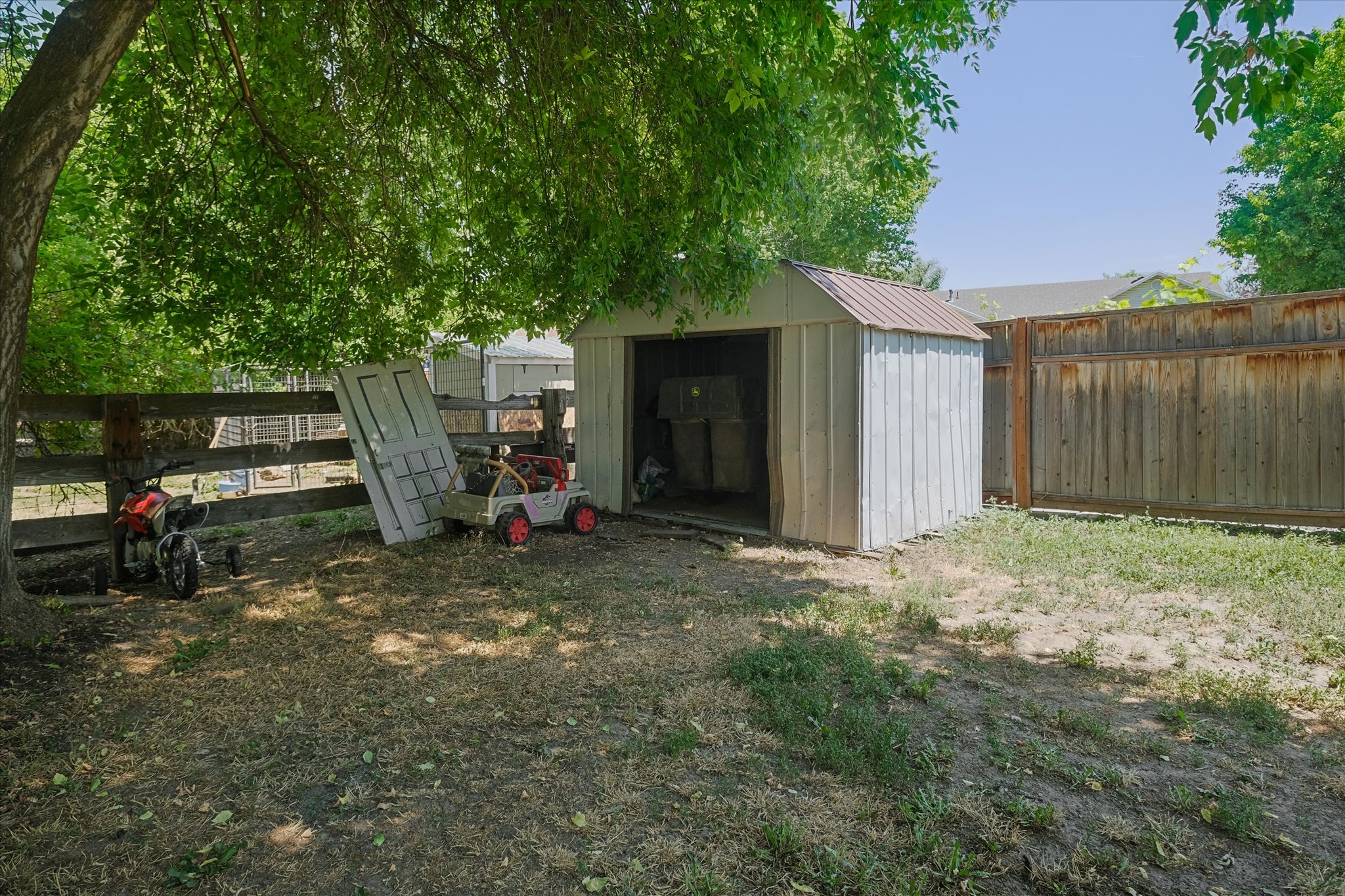 Backyard featuring a metal shed with a pitched roof, a wood fence, and mature trees providing shade