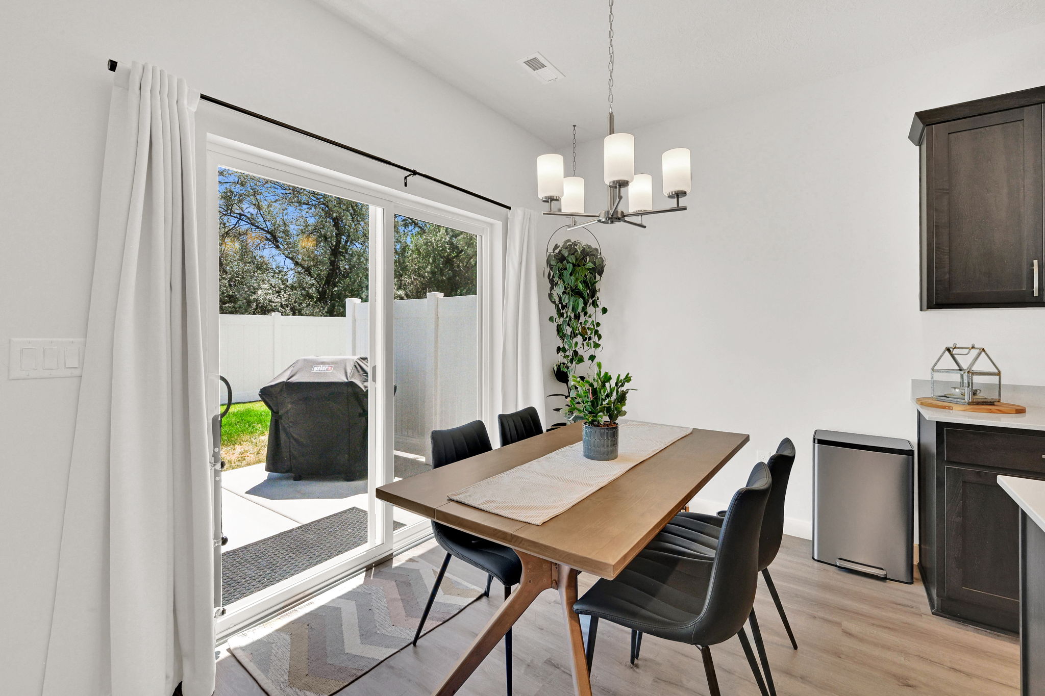 Dining area featuring wood-finish flooring, a contemporary chandelier, and a sliding glass door providing direct access to the concrete patio