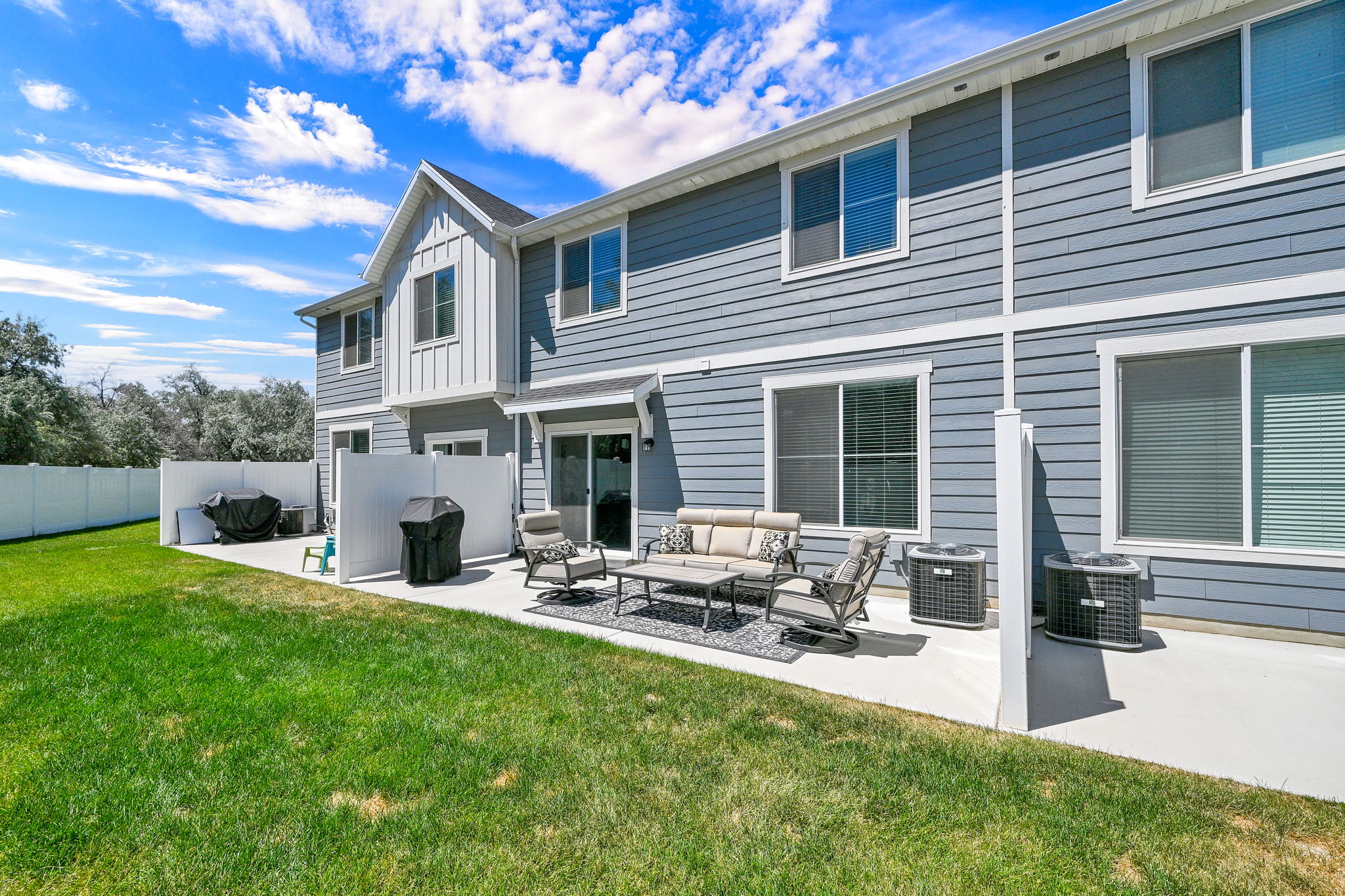 Rear exterior featuring a concrete patio, sliding glass door access, white privacy fencing, and two exterior HVAC units