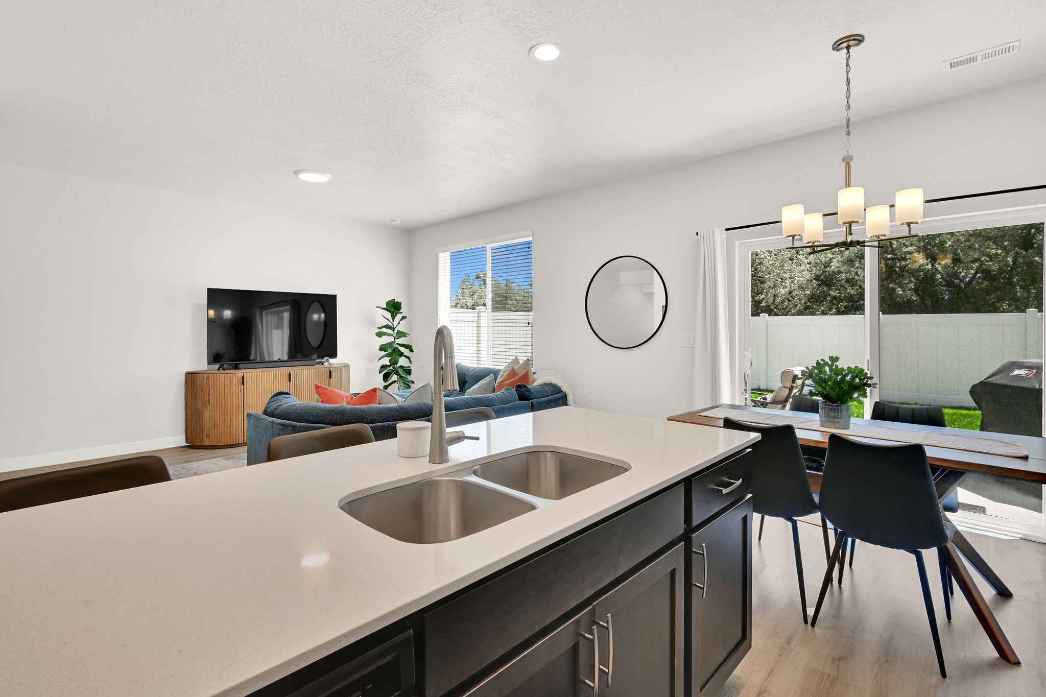 Open-concept living space featuring a kitchen island with dual stainless steel sinks, dark cabinetry, and light-toned countertops