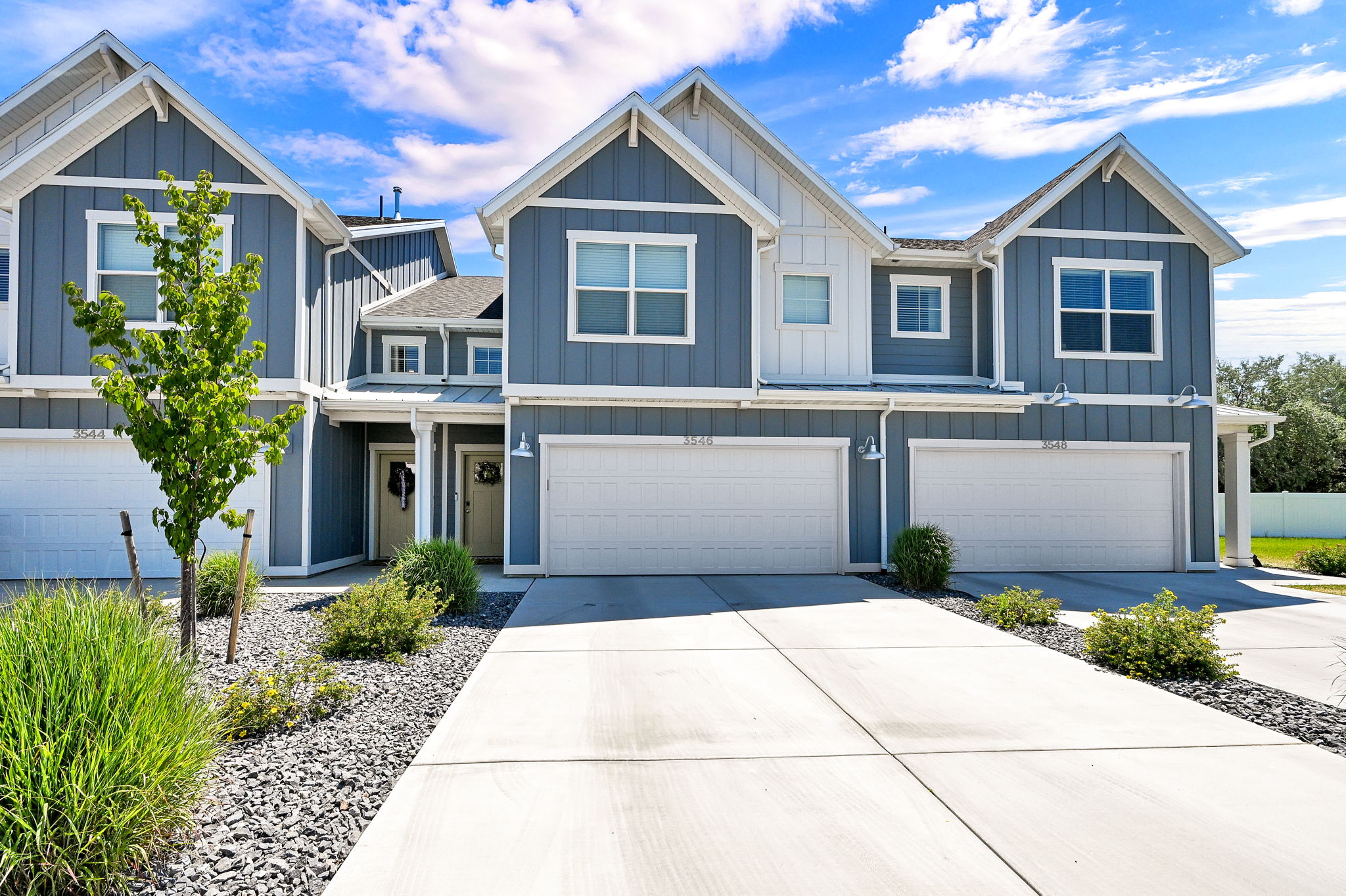 Modern townhome exterior featuring blue vertical siding, white trim, gabled roofs, and an attached two-car garage