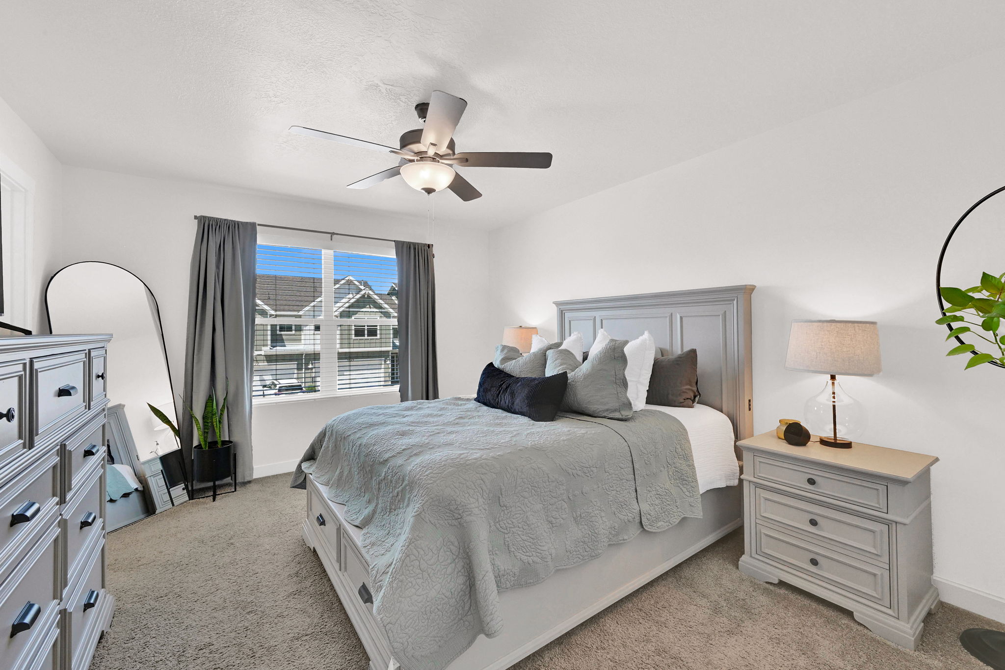 Carpeted room featuring a ceiling fan with integrated lighting, a large window with blinds and drapes, and a paneled headboard