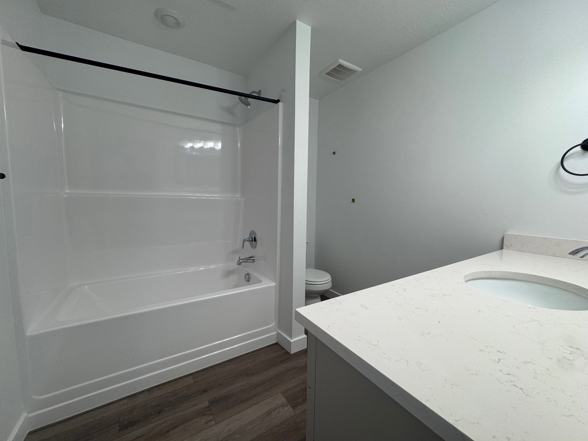Bathroom featuring a white tub-shower combination with a chrome faucet, a vanity with a light-colored countertop and an integrated sink, and wood-finish flooring