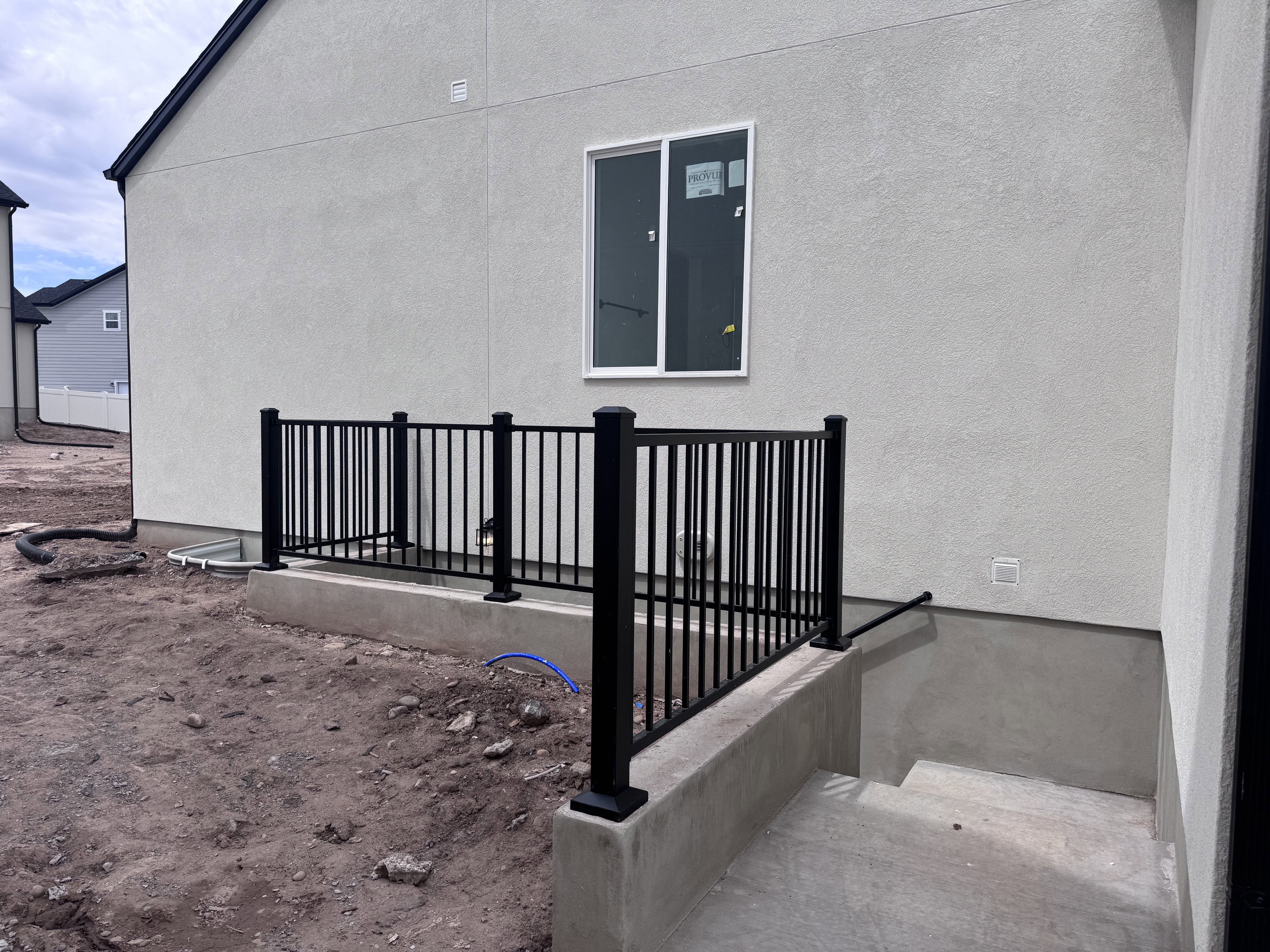 Exterior stucco finish with black aluminum railing leading to a concrete basement entry