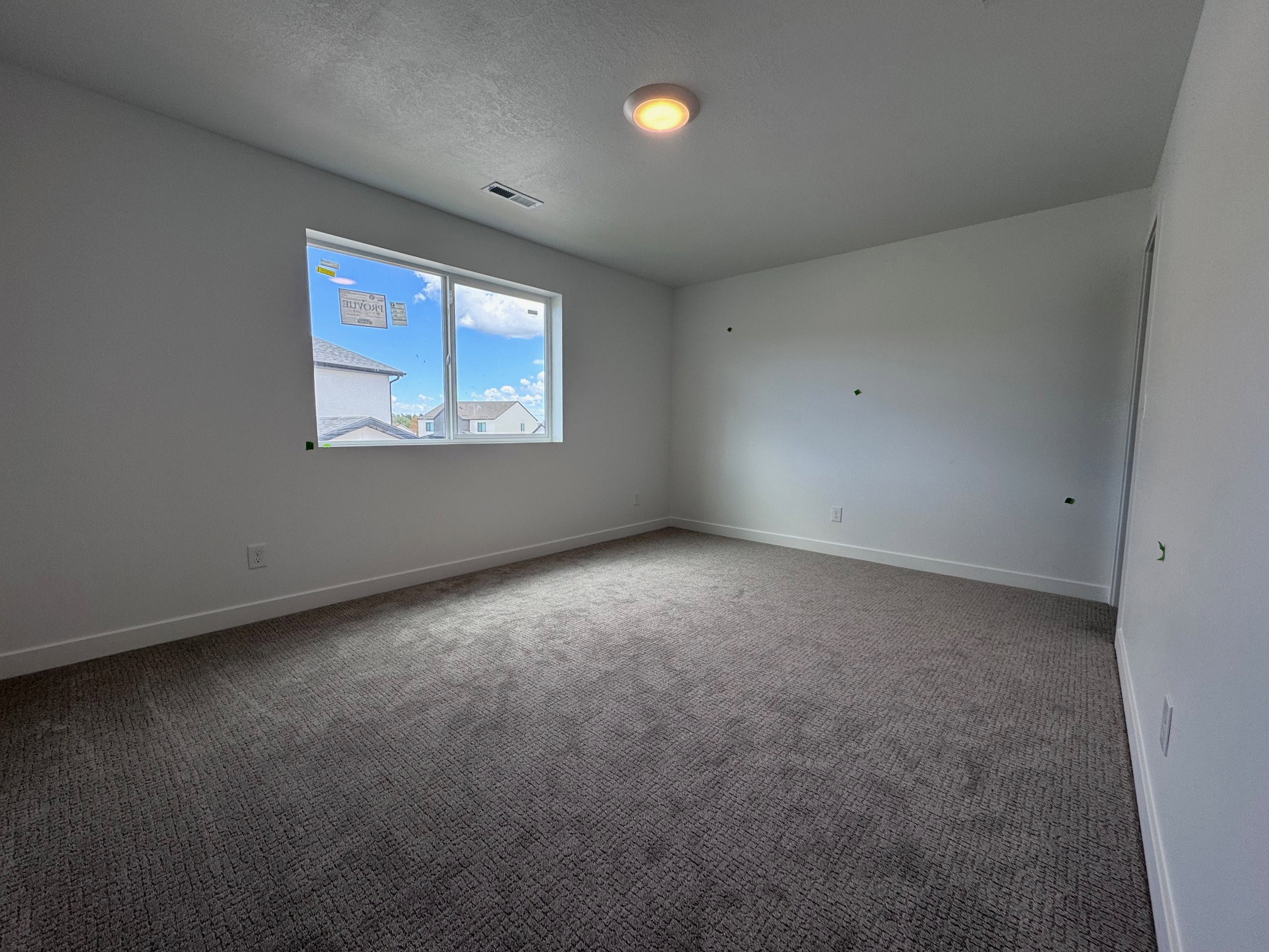 Spacious room featuring neutral carpeting, white walls, a large window, a ceiling-mounted light fixture, and white baseboards
