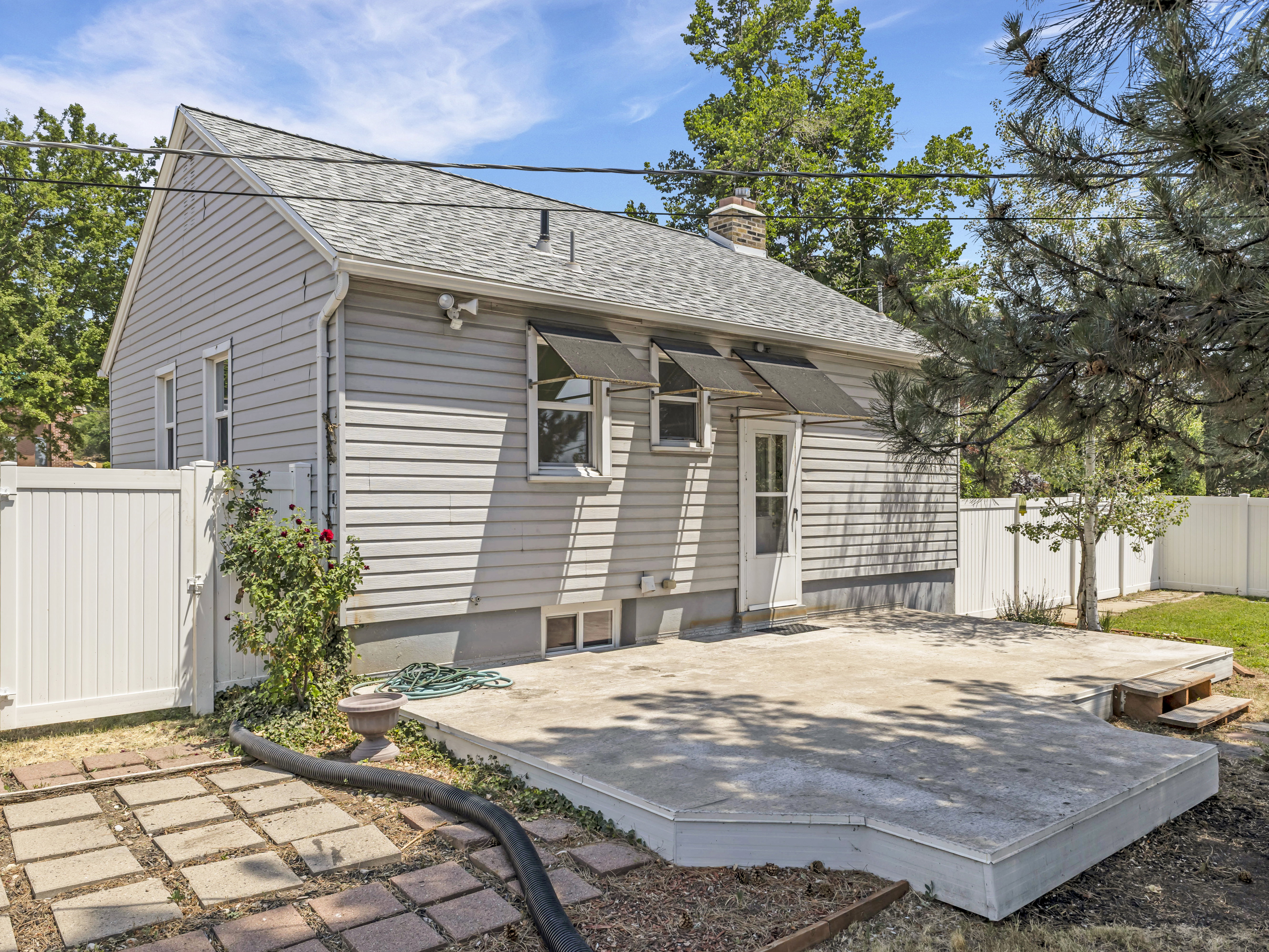 Rear exterior featuring light grey siding, a white screen door, and a concrete patio