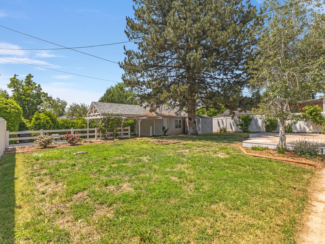 Grassy yard featuring a white picket fence, a covered arbor, and mature trees