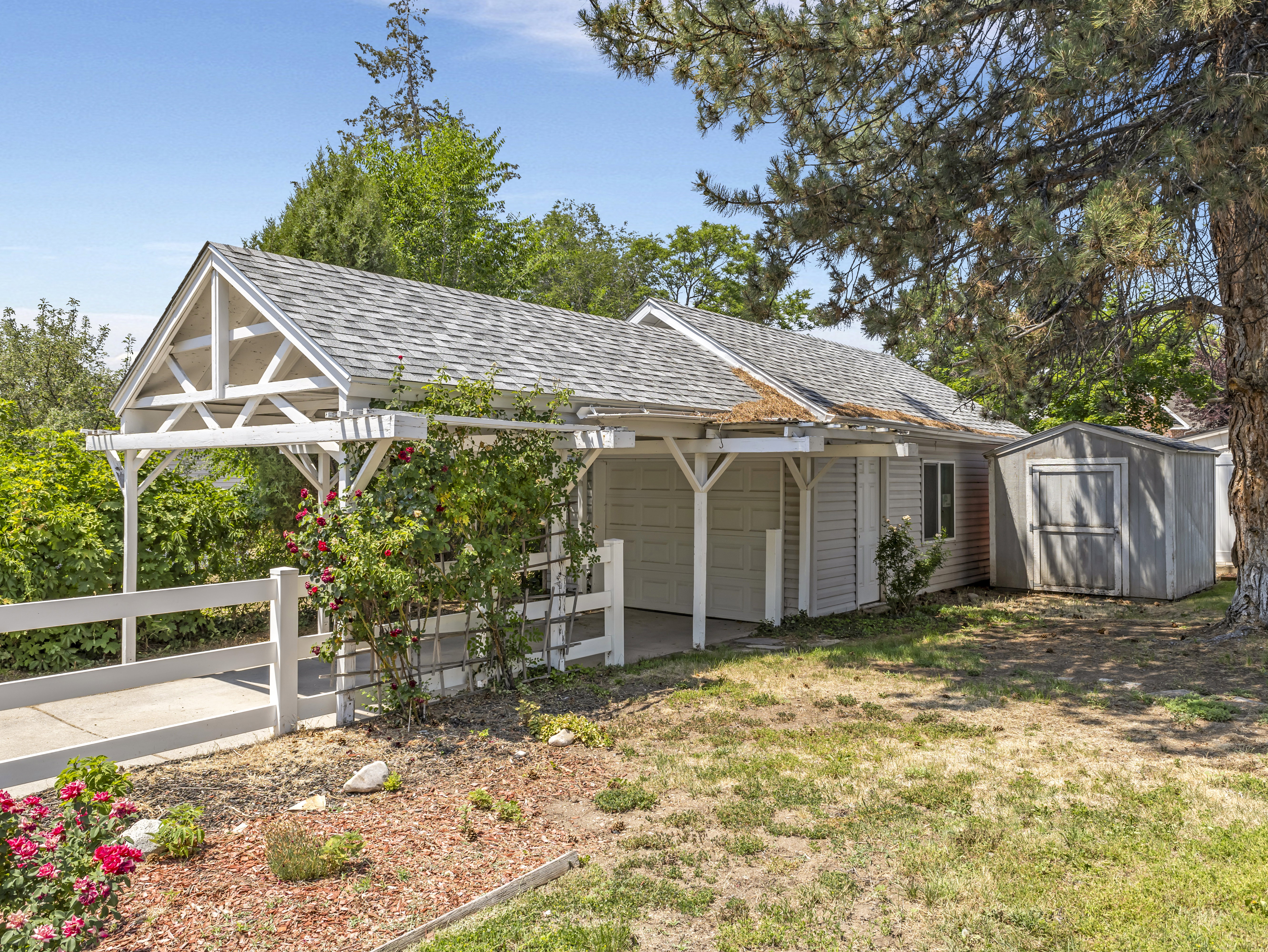 Carport with white pergola structure, asphalt shingle roofing, and white picket fencing