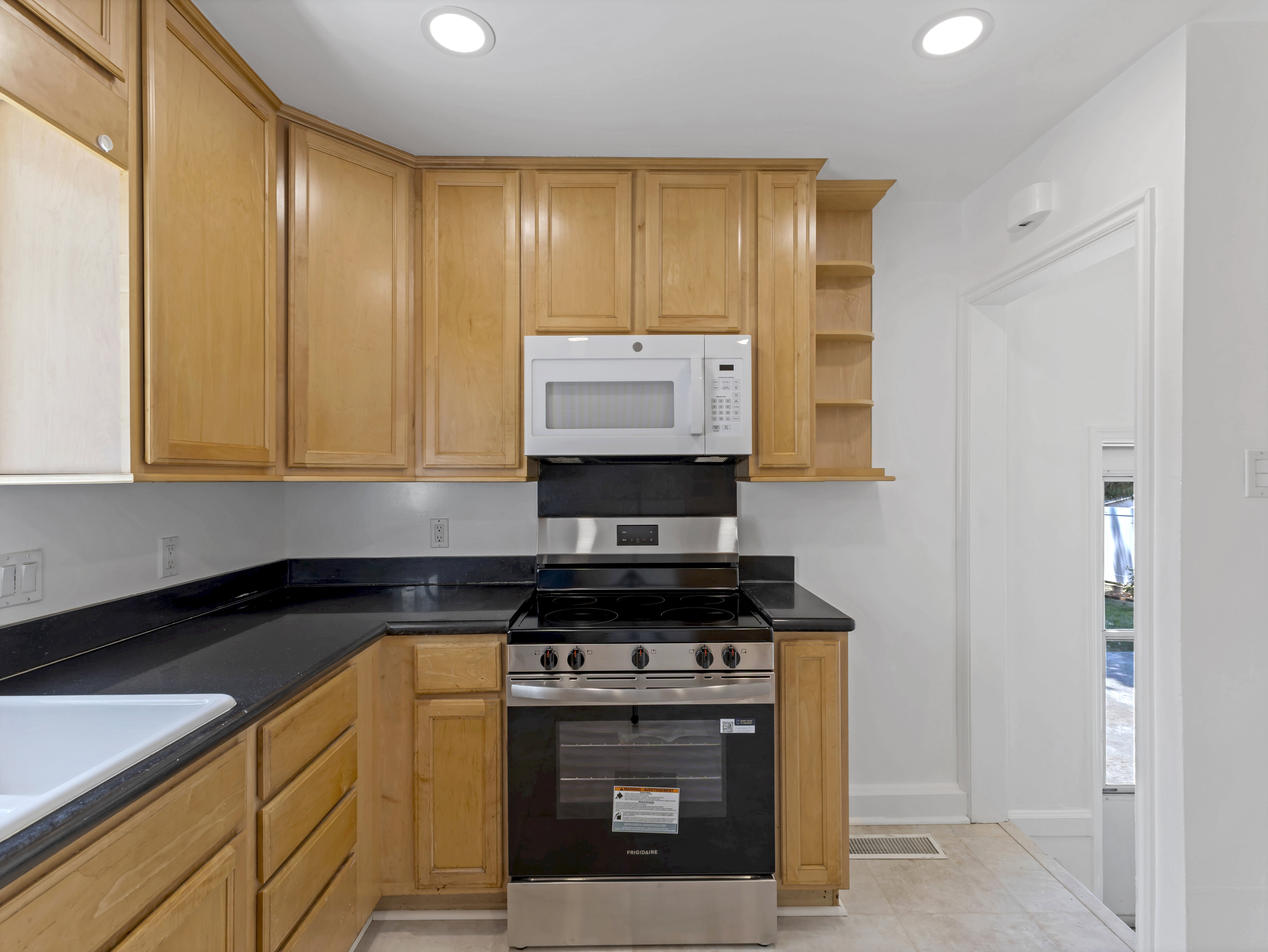 Kitchen featuring wood cabinetry, black countertops, stainless steel range with overhead microwave, and recessed lighting