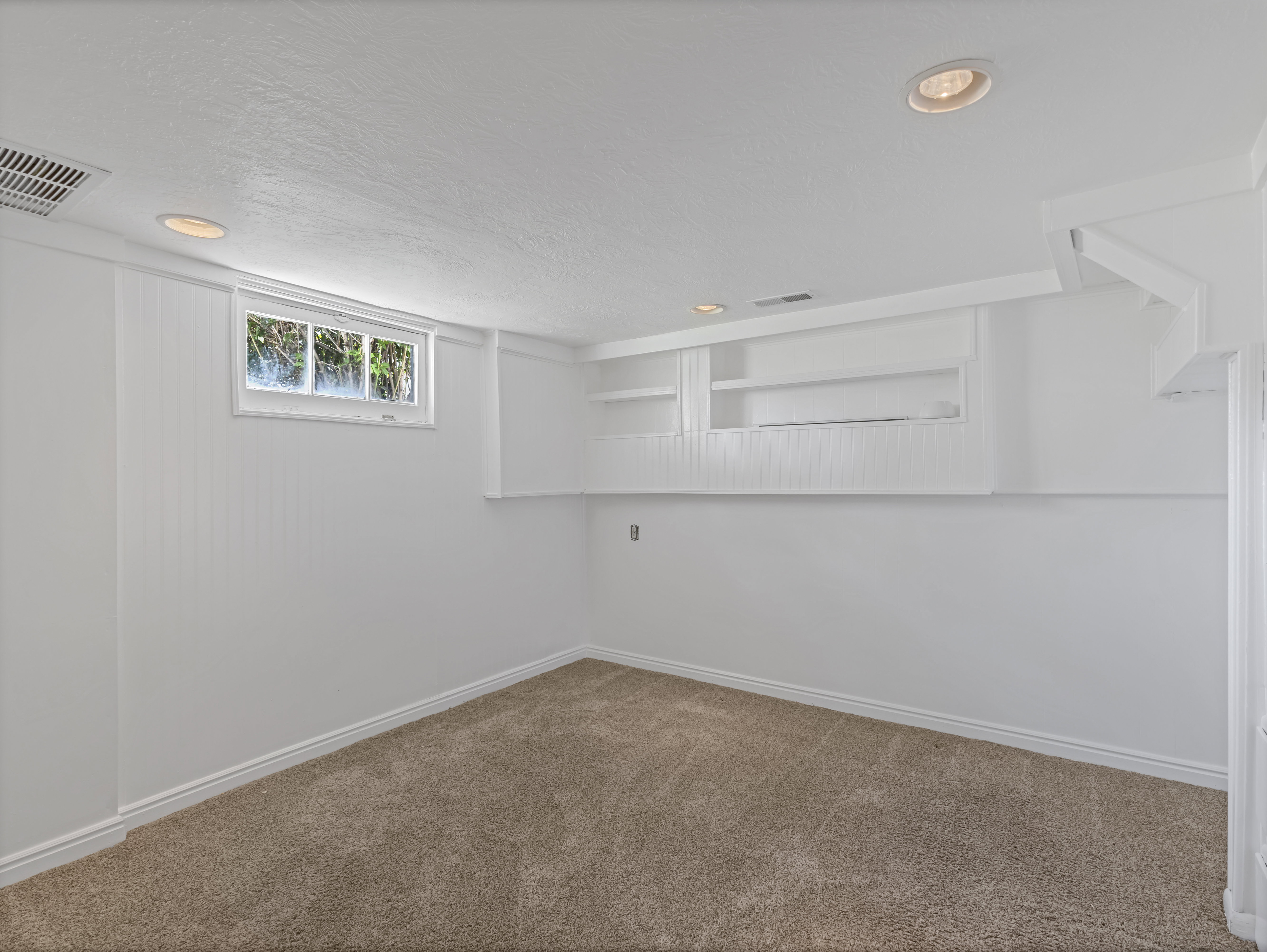Carpeted room featuring recessed lighting, a window, built-in shelving, white baseboards, and white paneling on a portion of the wall