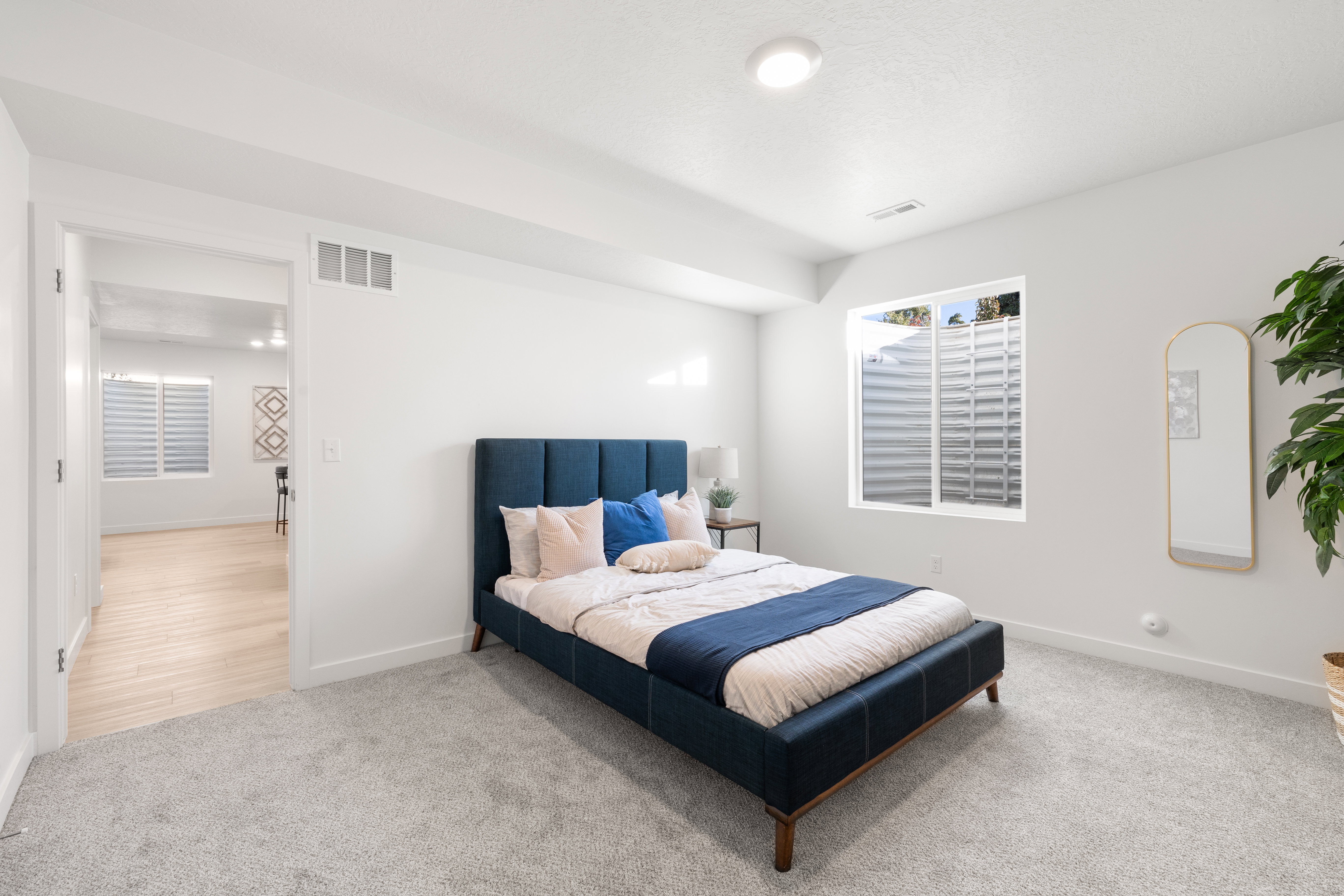 Carpeted bedroom with a recessed ceiling light, a large window with white horizontal blinds, and white walls