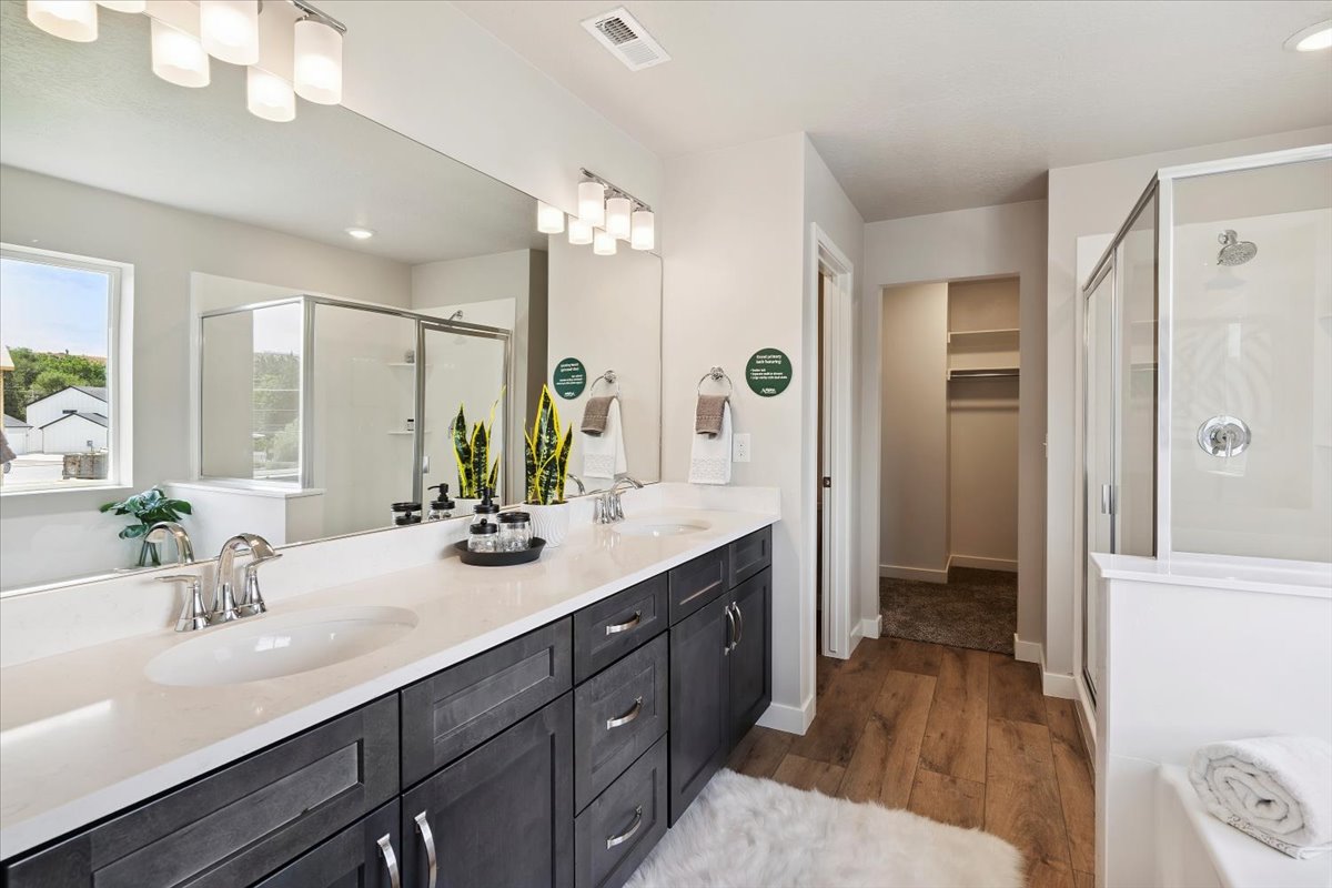 Double vanity with a white countertop and dark cabinetry, large mirror, and wood-finish flooring