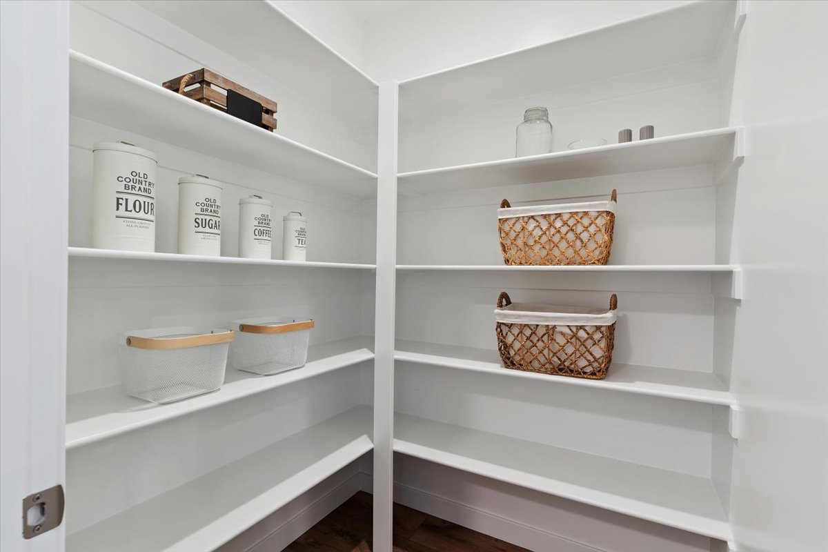 Spacious corner pantry featuring multiple white shelves, a white door frame, and dark wood-finish flooring