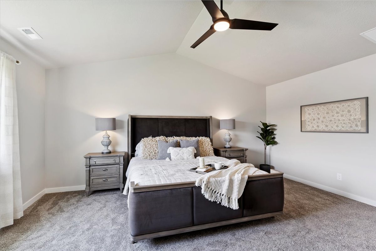 Carpeted bedroom featuring a vaulted ceiling with a ceiling fan, white walls, and a large window with sheer curtains