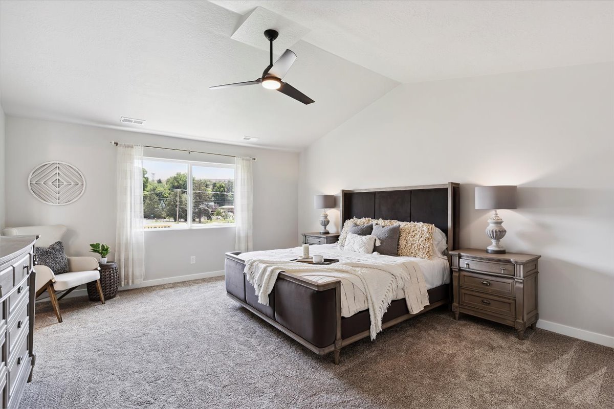 Spacious bedroom with vaulted ceilings, a large window, light gray carpeting, and a ceiling fan
